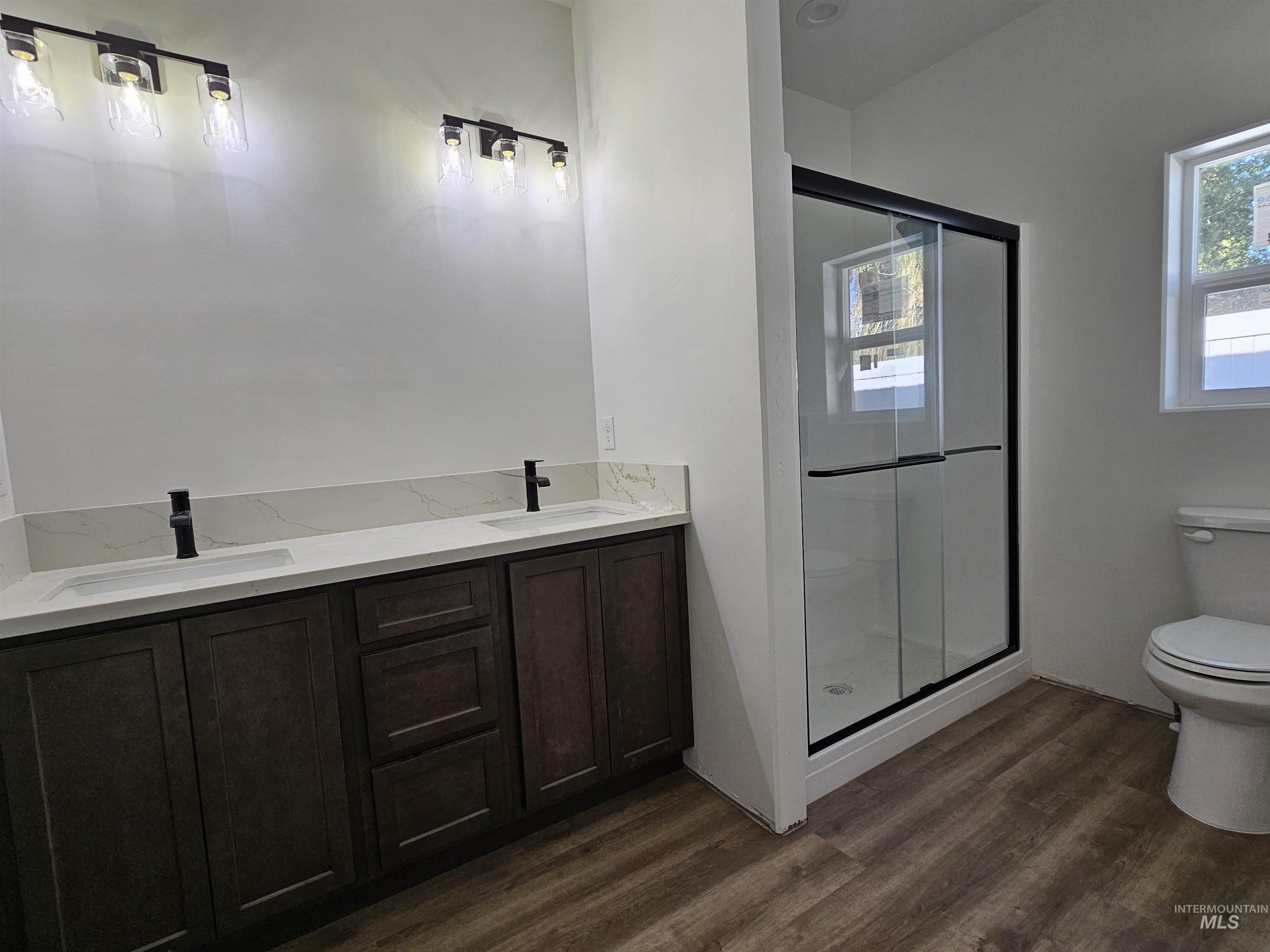 Full bathroom featuring dark wood-style floors, double vanity, and a shower stall