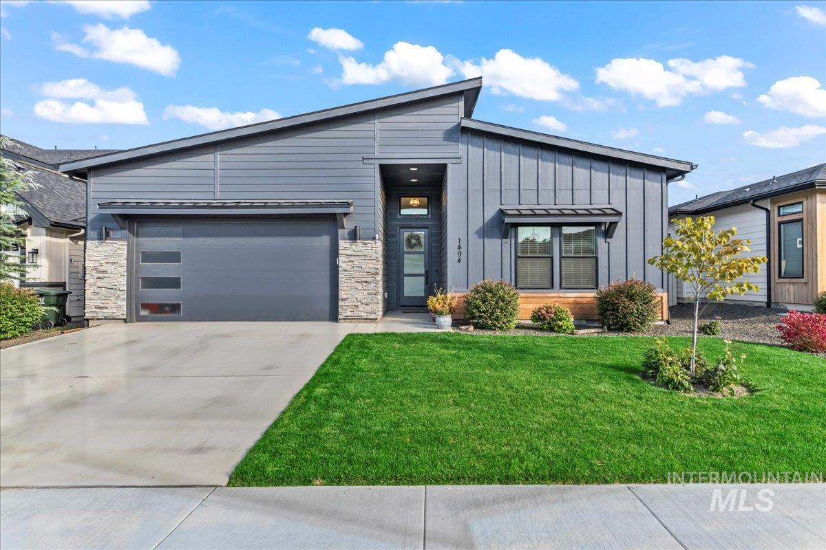 View of front facade featuring board and batten siding, driveway, a front lawn, and stone siding