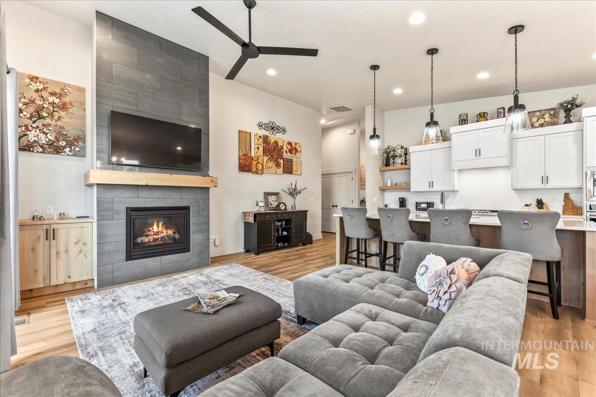 Living area featuring a tiled fireplace, light wood-style flooring, a ceiling fan, and recessed lighting
