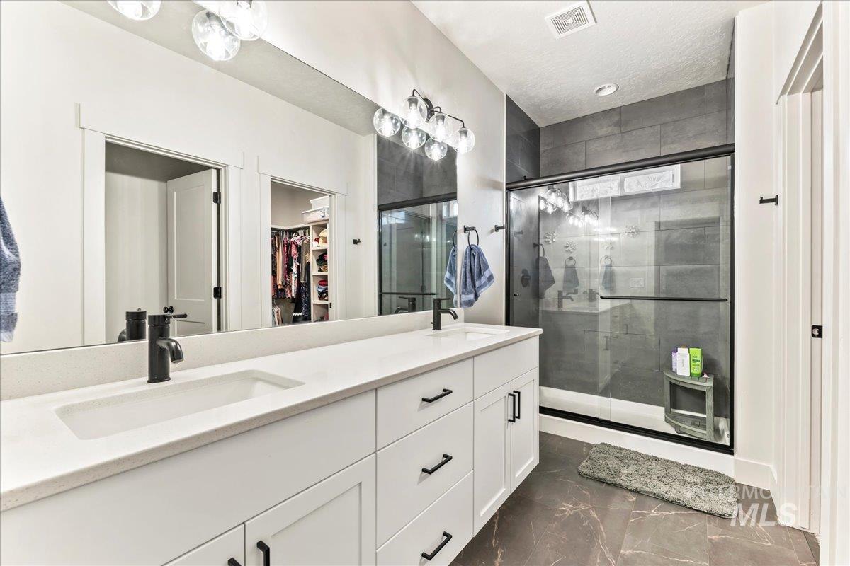 Bathroom featuring a walk in closet, double vanity, a stall shower, dark marble finish flooring, and a textured ceiling