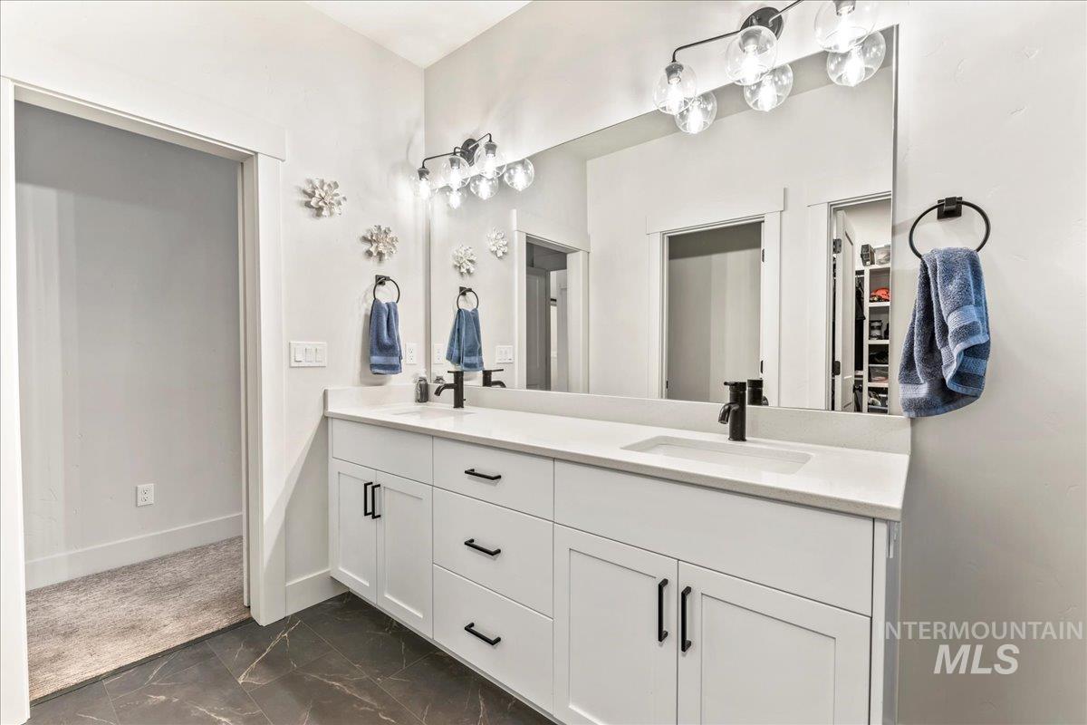 Bathroom featuring double vanity, dark marble finish flooring, and a walk in closet