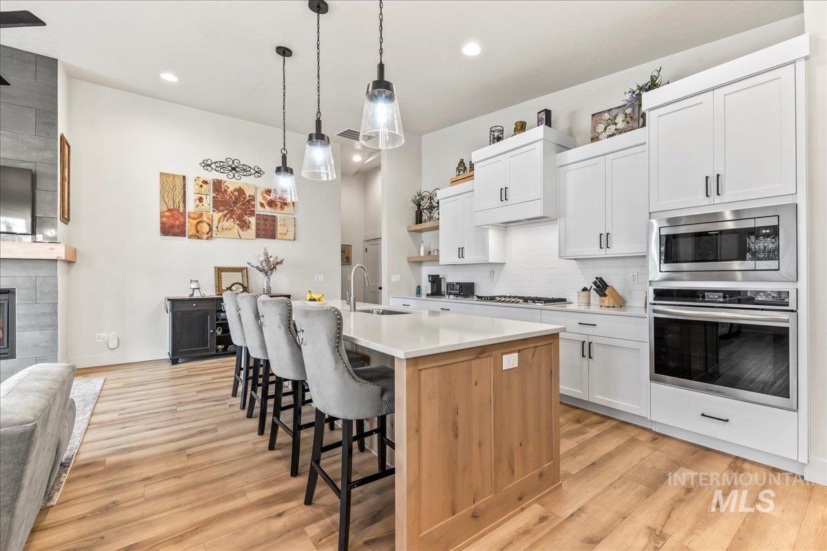 Kitchen with appliances with stainless steel finishes, white cabinetry, tasteful backsplash, a breakfast bar area, and light wood-type flooring