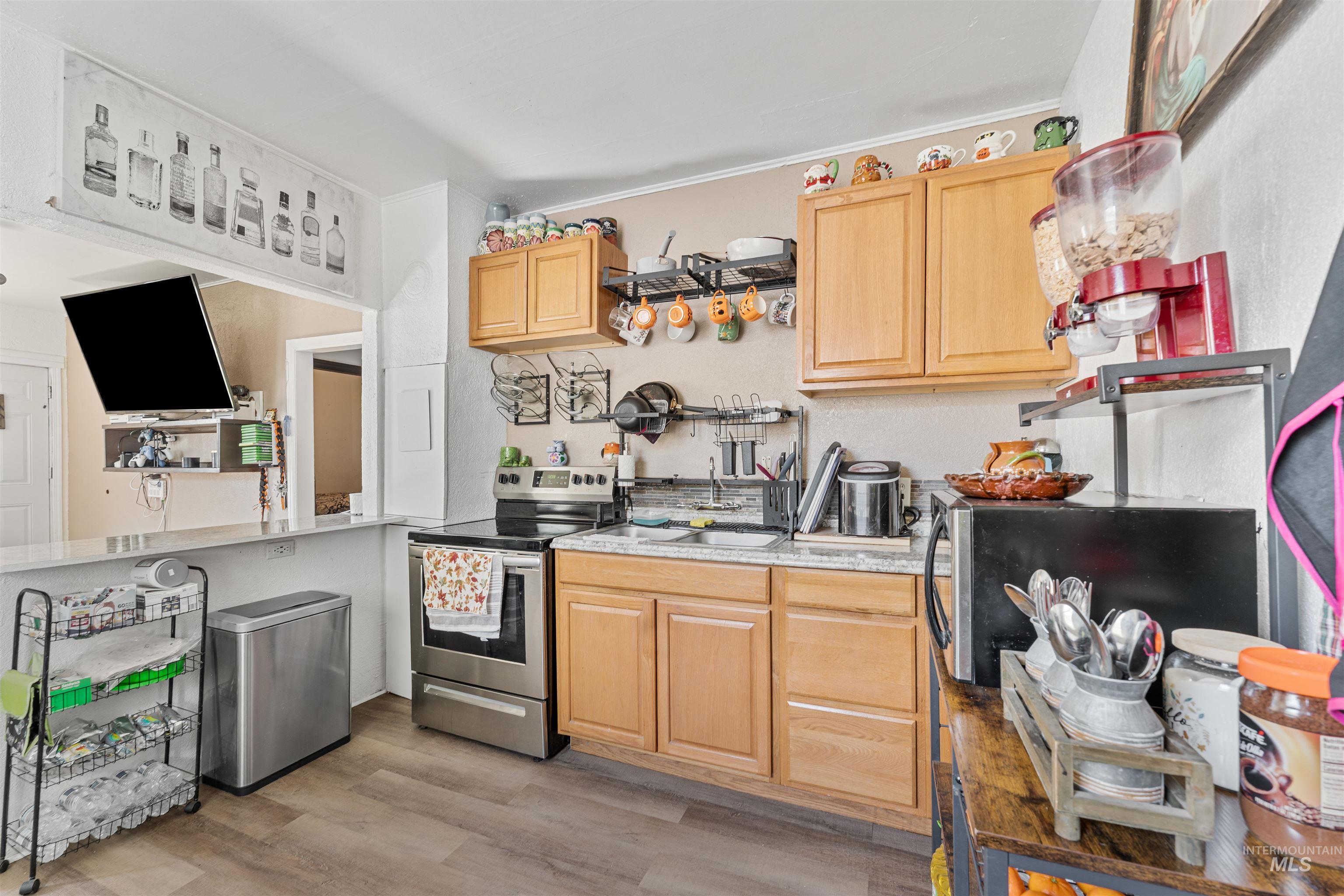 Kitchen featuring stainless steel electric range oven, light brown cabinets, light wood-style floors, light stone counters, and ornamental molding