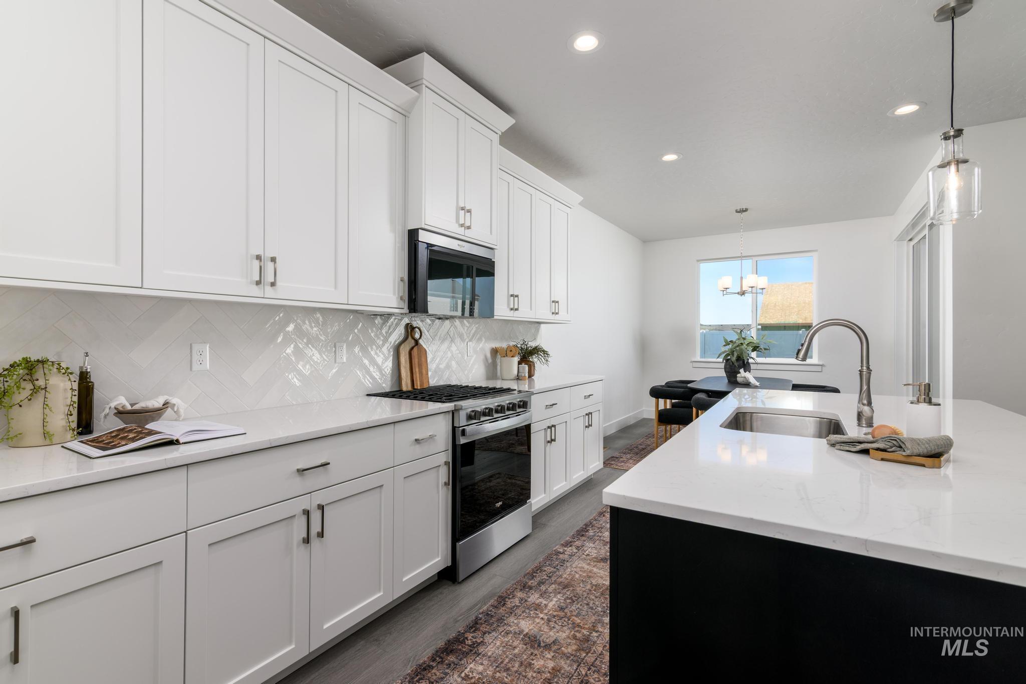 Kitchen with appliances with stainless steel finishes, hanging light fixtures, light stone countertops, recessed lighting, and white cabinetry