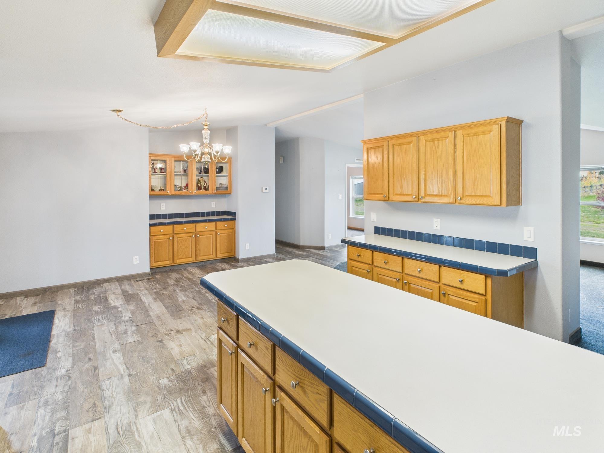 Kitchen with light wood-style floors, tile countertops, a chandelier, brown cabinetry, and vaulted ceiling