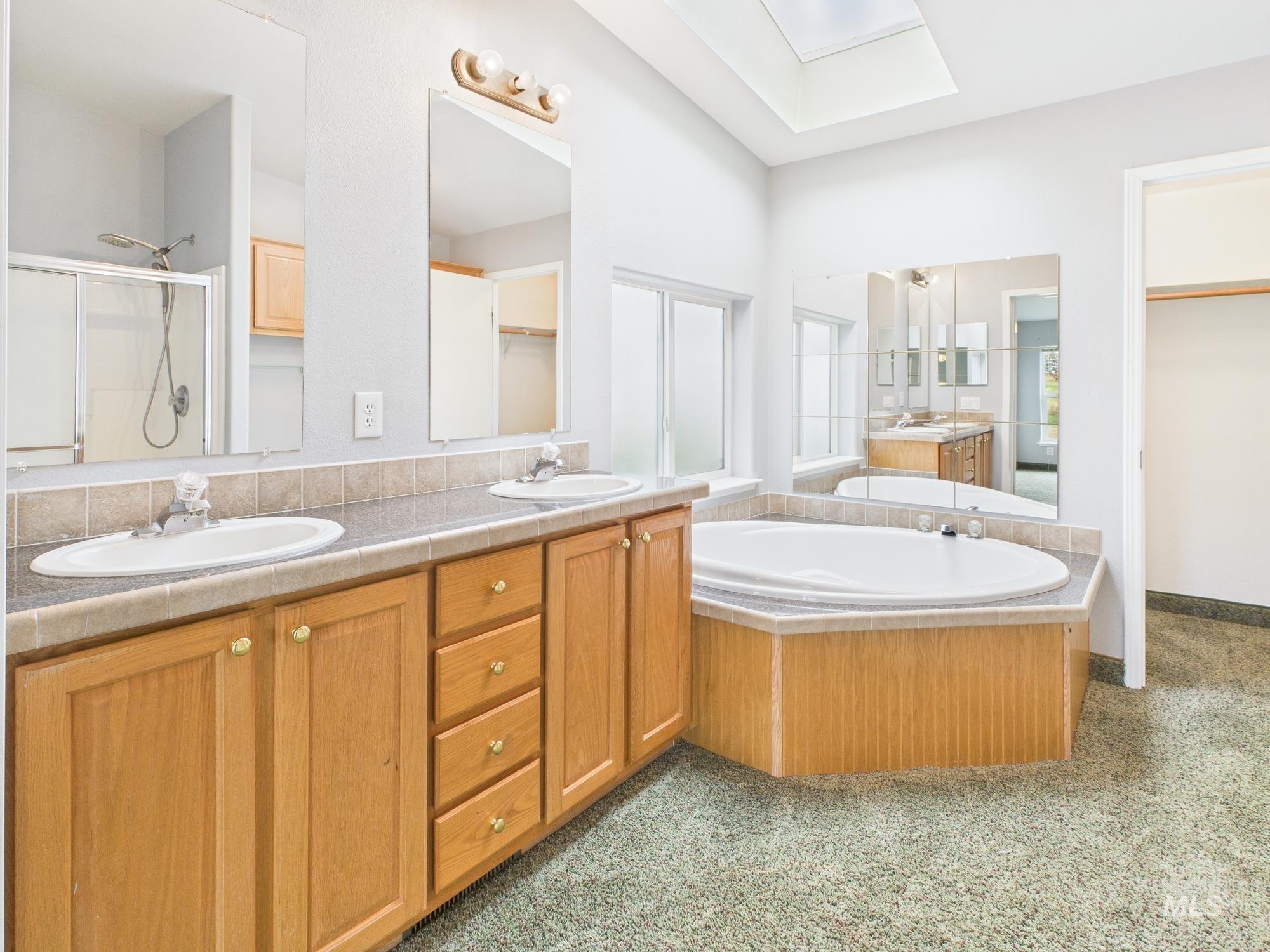 Bathroom featuring a stall shower, double vanity, a bath, a skylight, and a closet