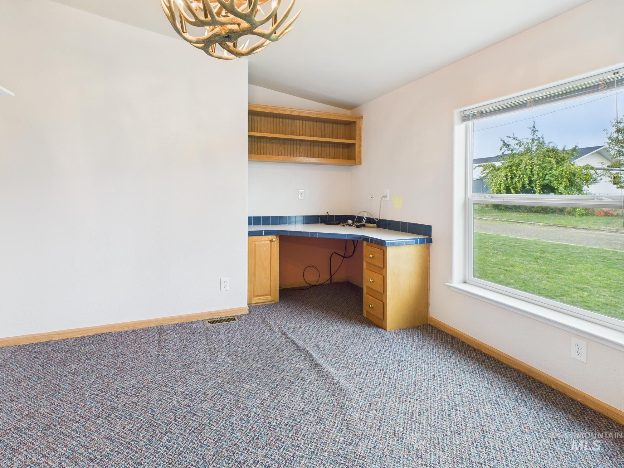 Unfurnished office with built in desk, vaulted ceiling, dark carpet, and a chandelier