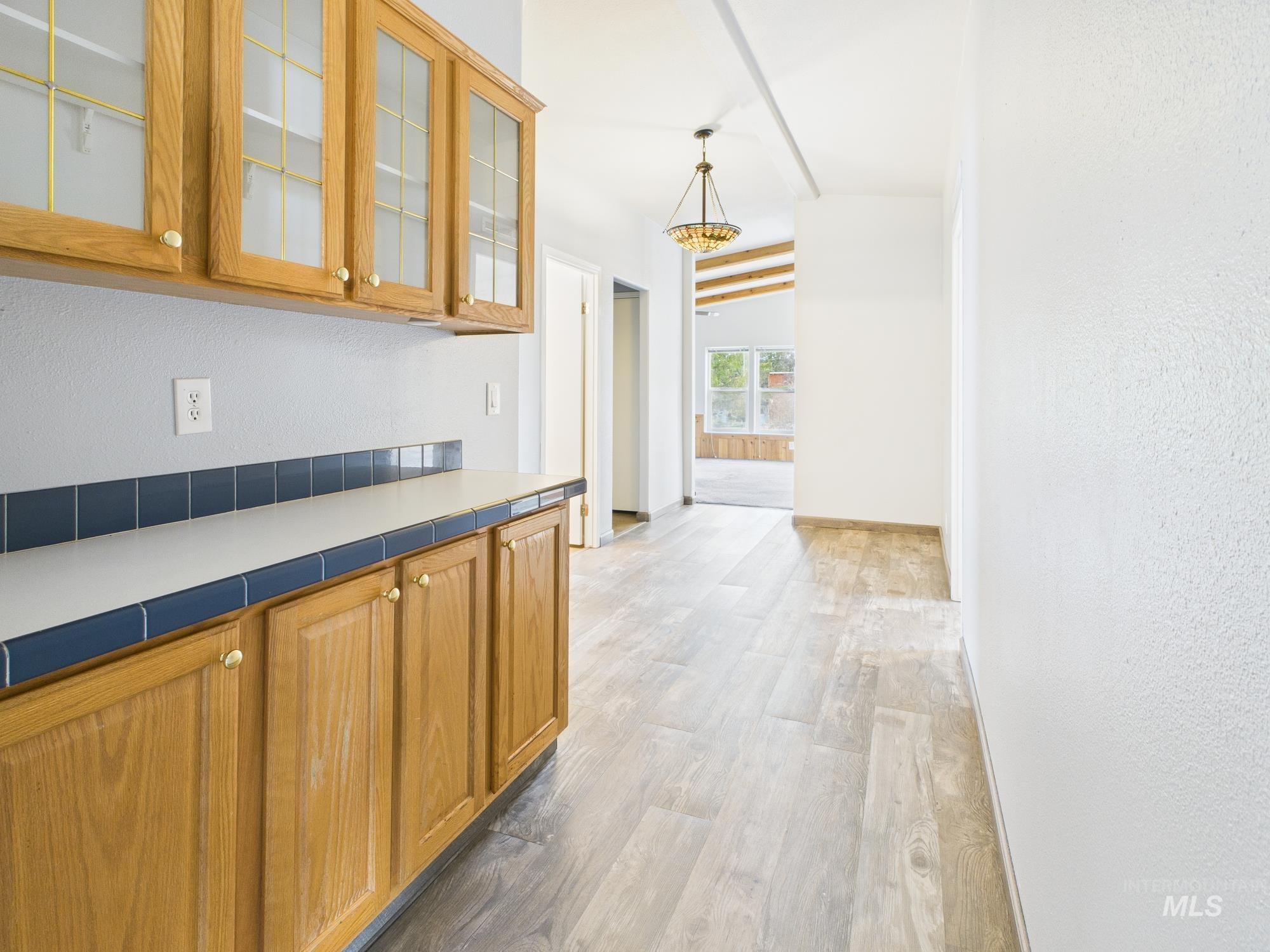 Corridor featuring a textured wall, light wood finished floors, vaulted ceiling, and a chandelier