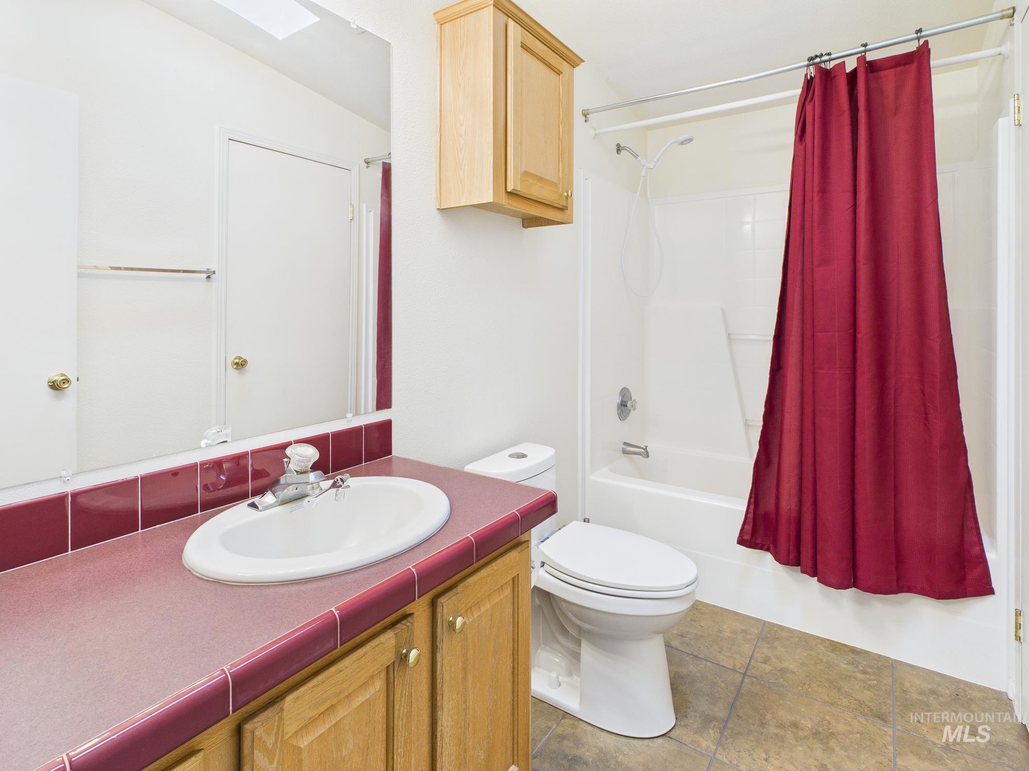 Full bathroom with shower / bath combo with shower curtain, a skylight, vanity, and light tile patterned flooring