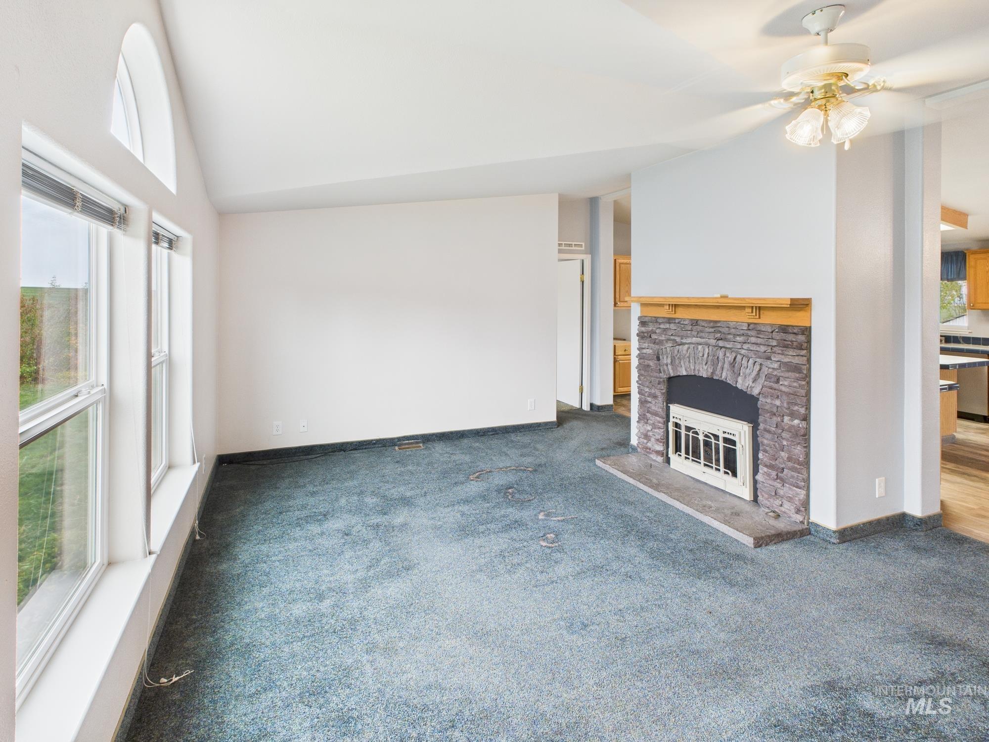 Unfurnished living room with vaulted ceiling, a stone fireplace, carpet, and a ceiling fan