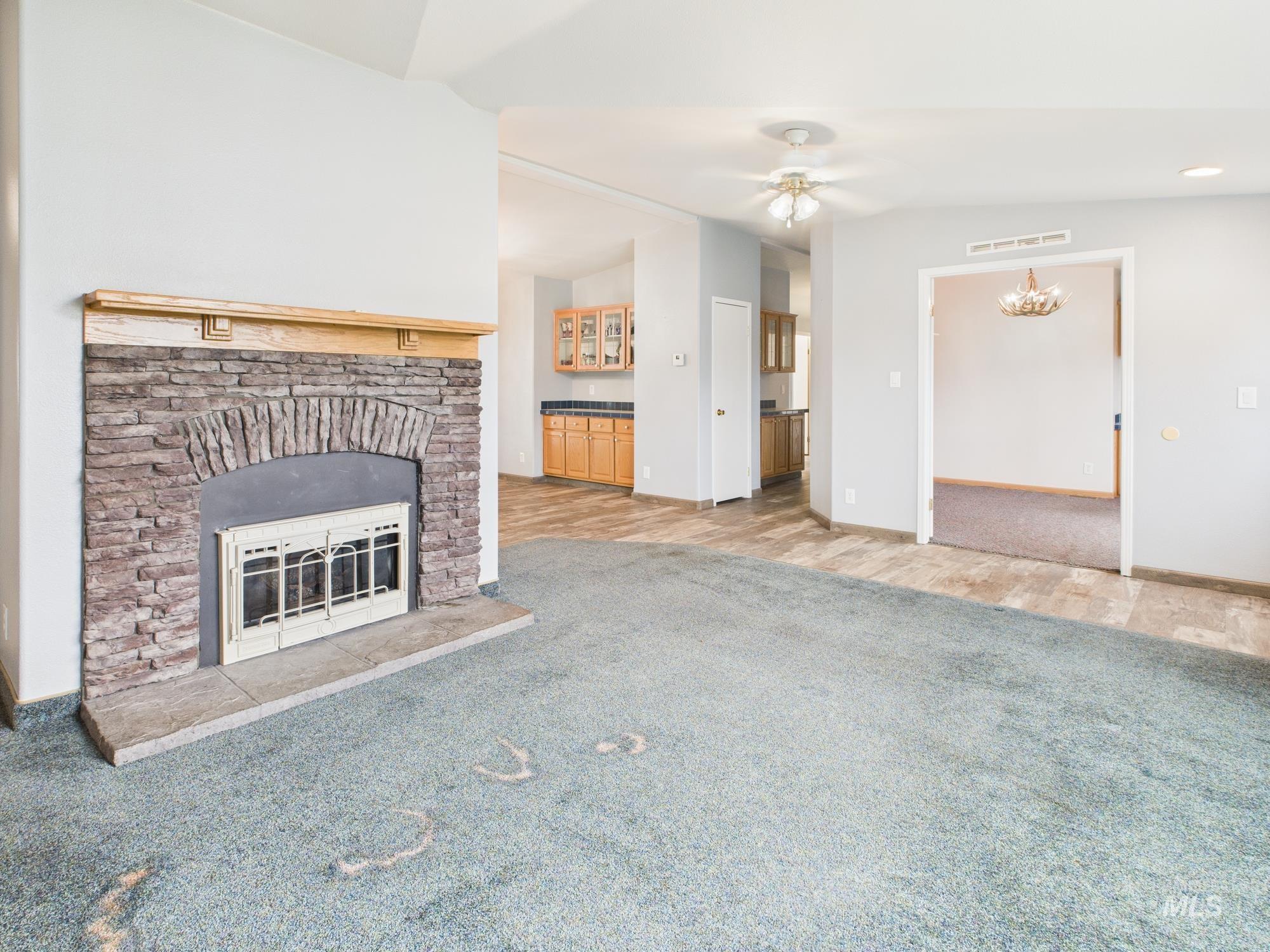 Unfurnished living room featuring carpet floors, a fireplace, a ceiling fan, vaulted ceiling, and a chandelier
