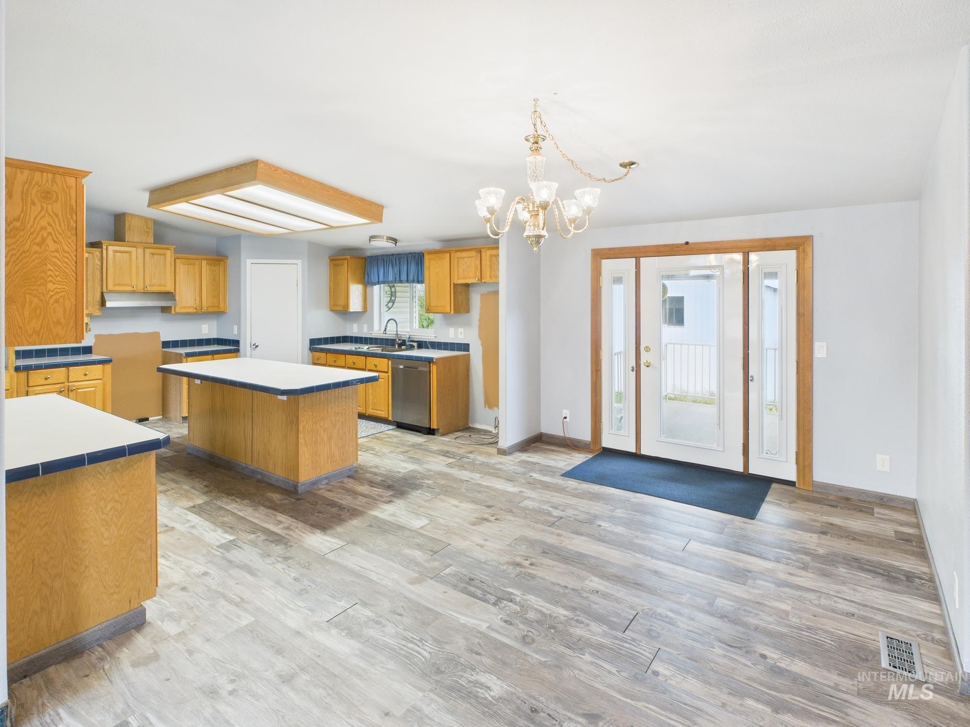 Kitchen with a kitchen island, a chandelier, light wood-style floors, stainless steel dishwasher, and pendant lighting
