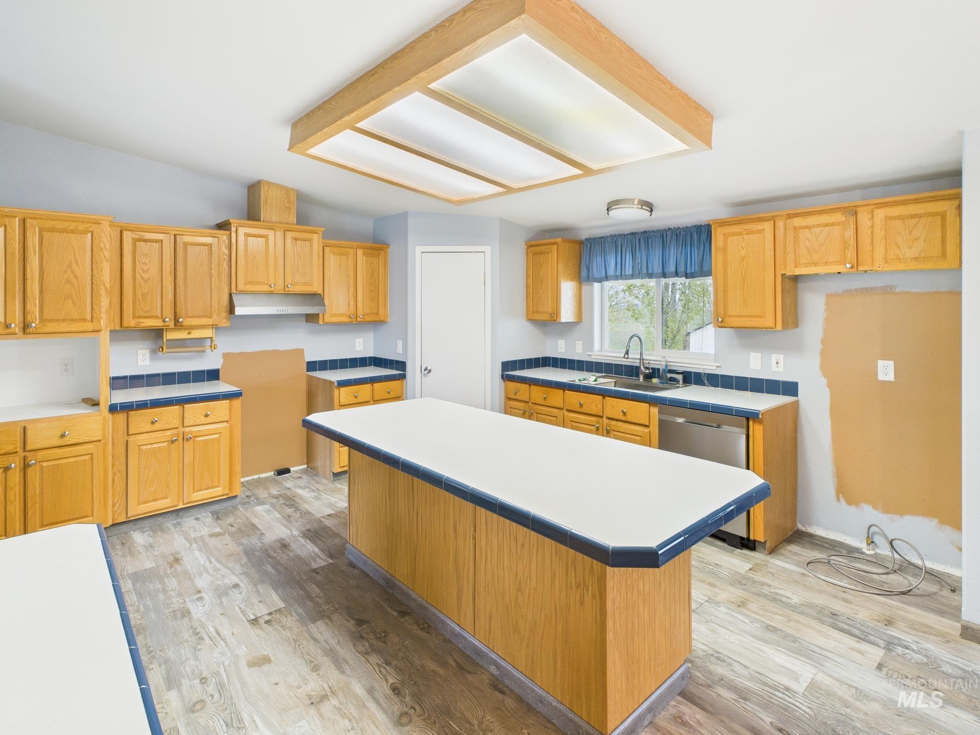 Kitchen featuring light wood-style flooring, dishwasher, a kitchen island, and light countertops