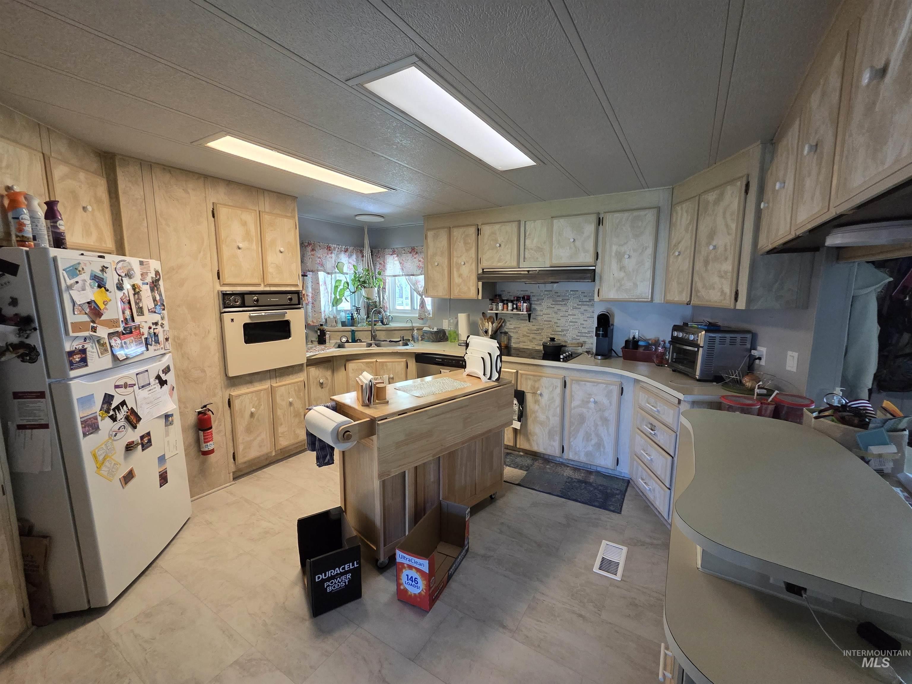 Kitchen with freestanding refrigerator, light countertops, backsplash, and light brown cabinets