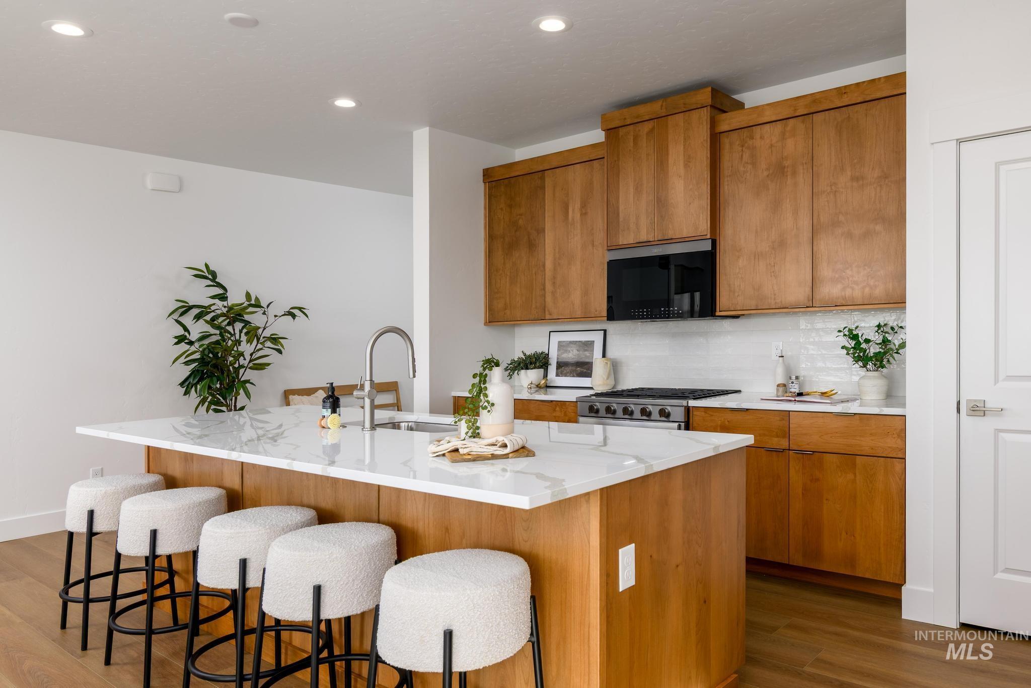 Kitchen with brown cabinets, decorative backsplash, dark wood-style flooring, a kitchen island with sink, and recessed lighting