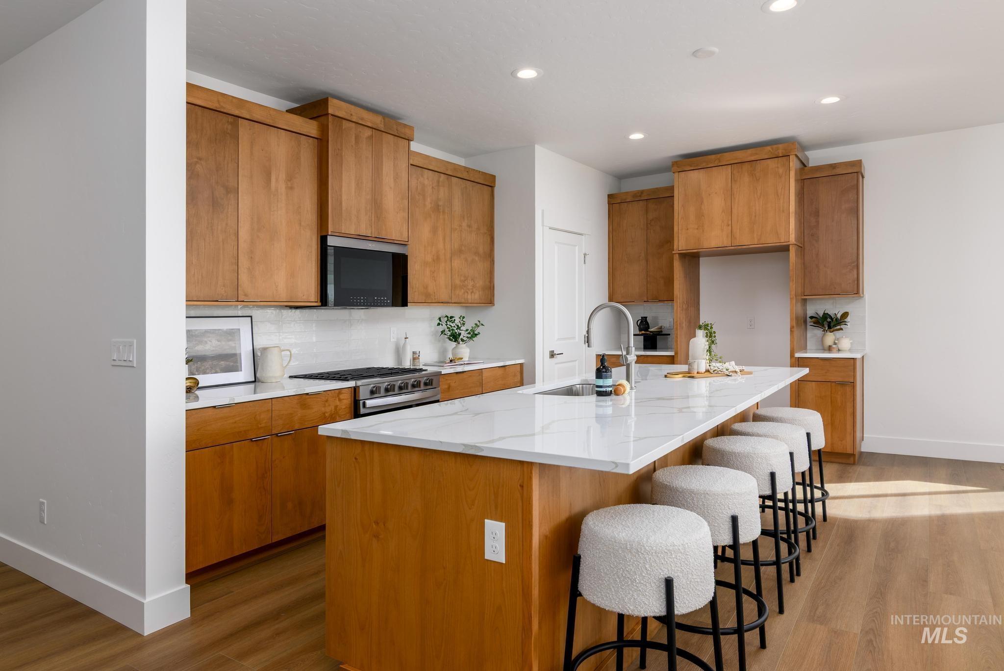 Kitchen featuring brown cabinets, backsplash, light stone counters, light wood-type flooring, and recessed lighting