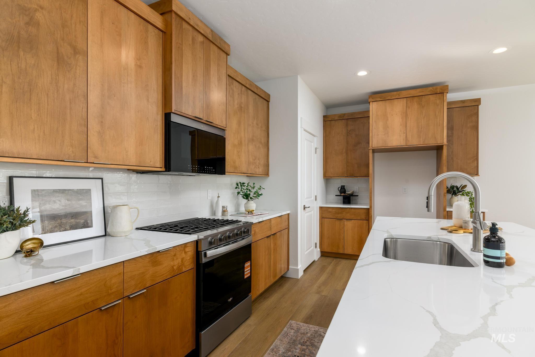 Kitchen featuring gas stove, brown cabinetry, dark wood-style flooring, light stone counters, and tasteful backsplash