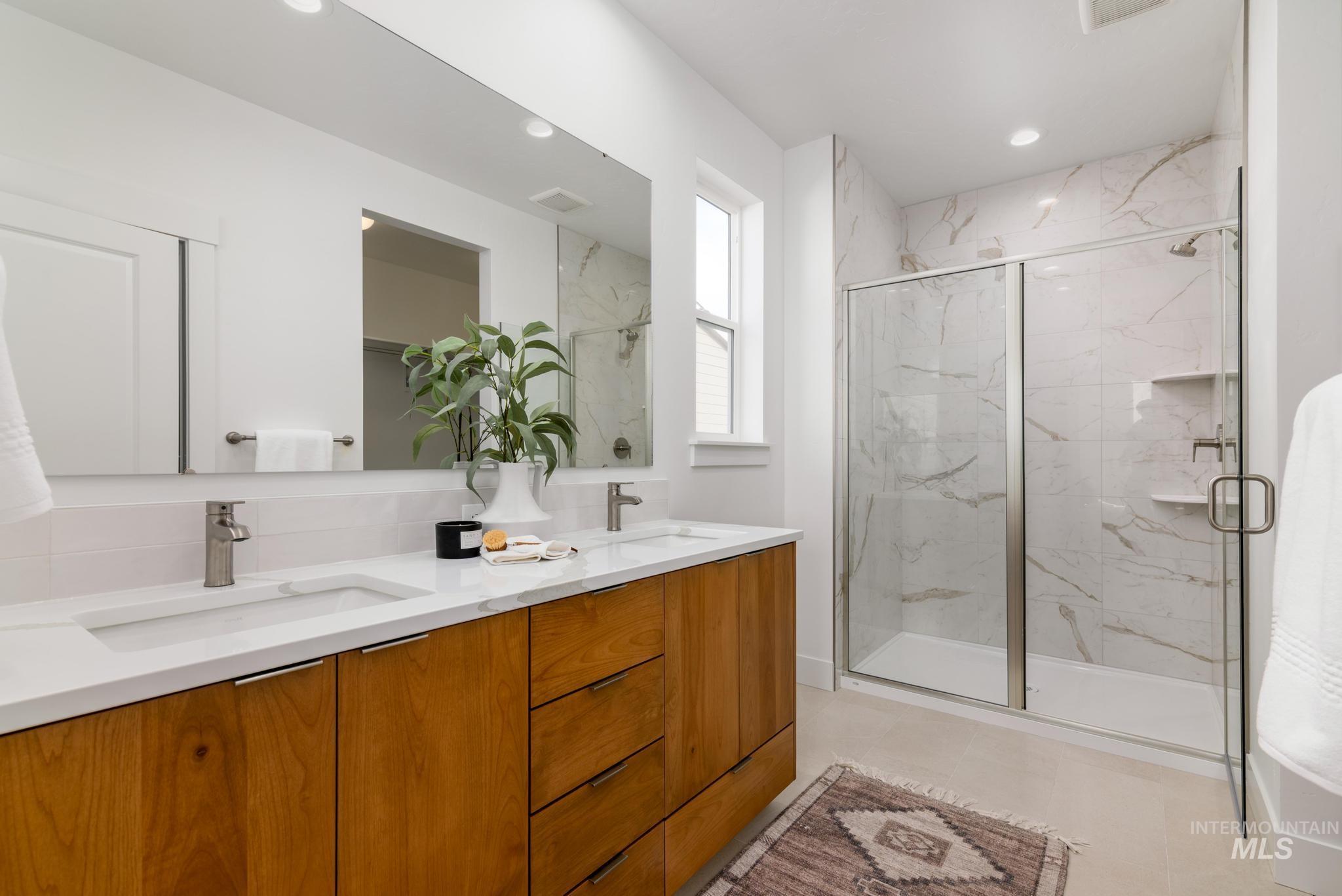 Full bath featuring a marble finish shower, double vanity, light tile patterned floors, and recessed lighting