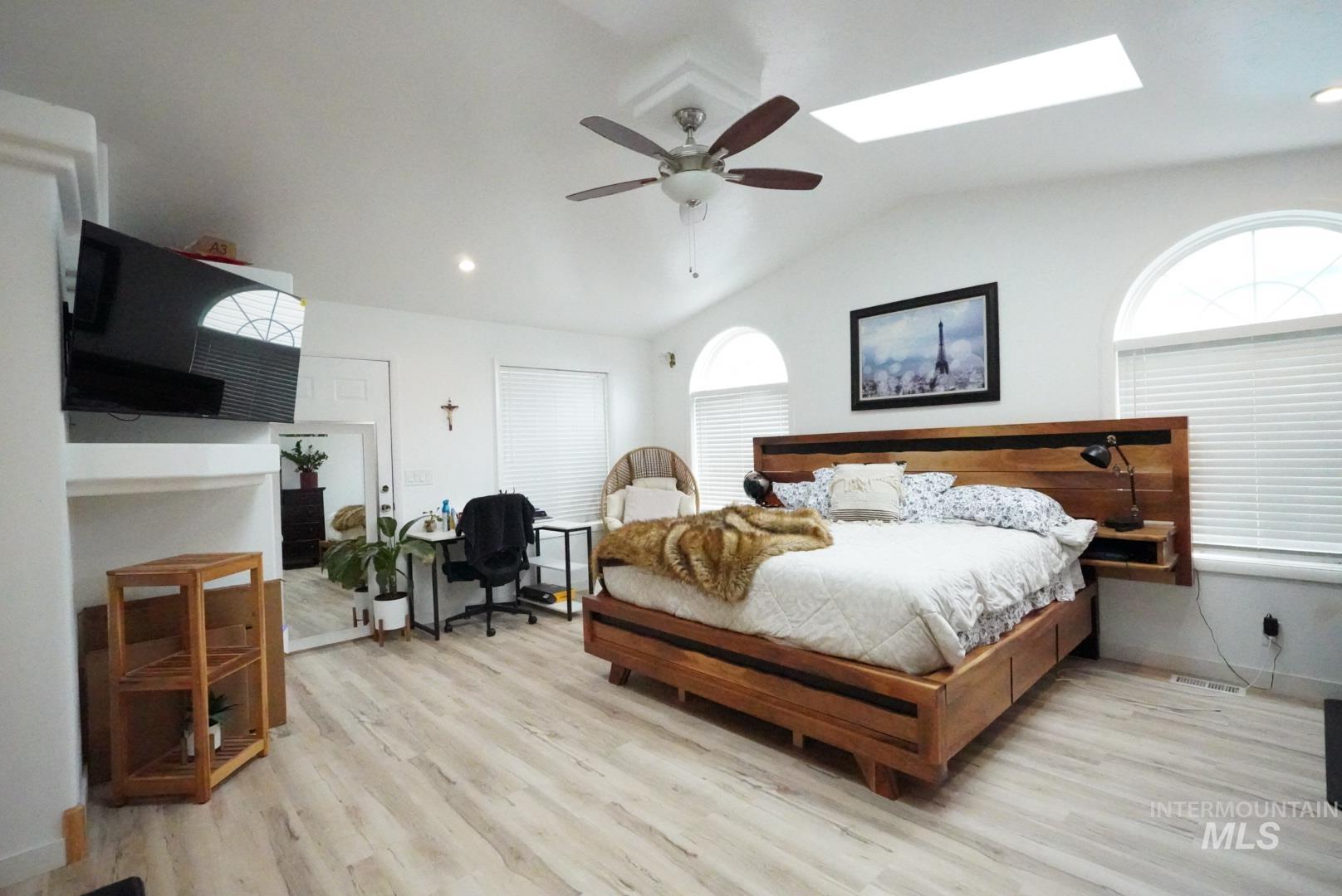 Bedroom with lofted ceiling, a skylight, light wood finished floors, multiple windows, and a ceiling fan