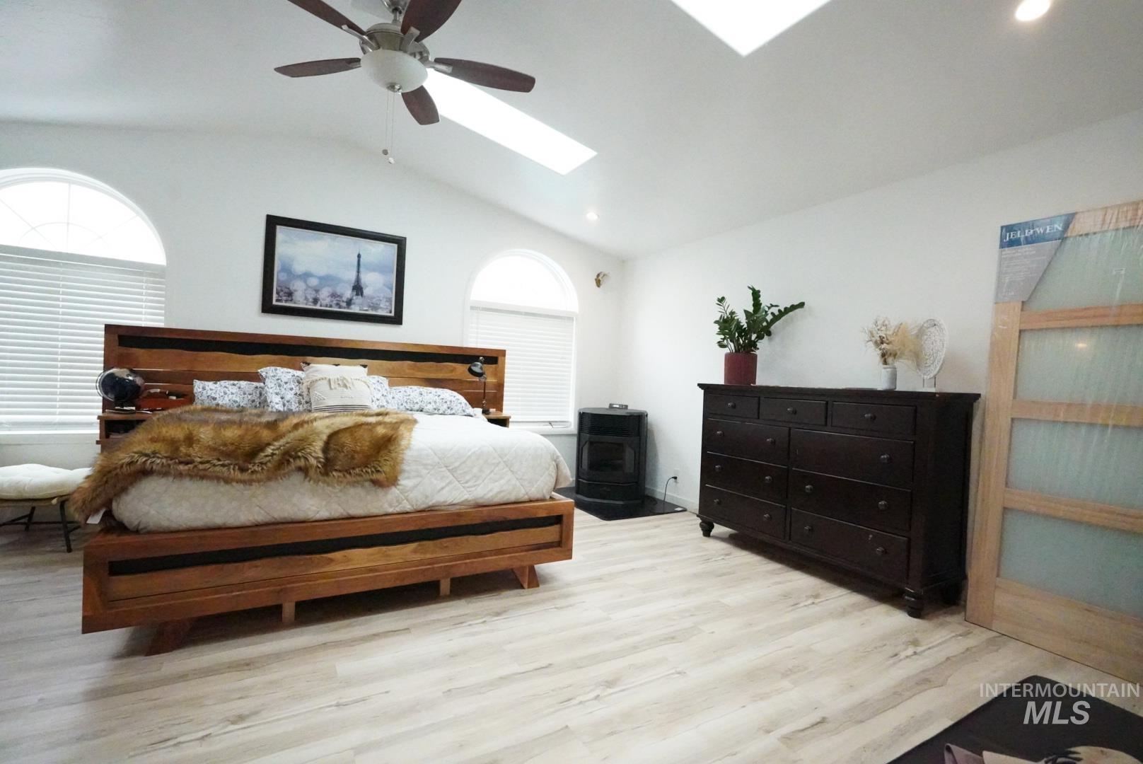 Bedroom featuring lofted ceiling, a skylight, light wood-style floors, and ceiling fan