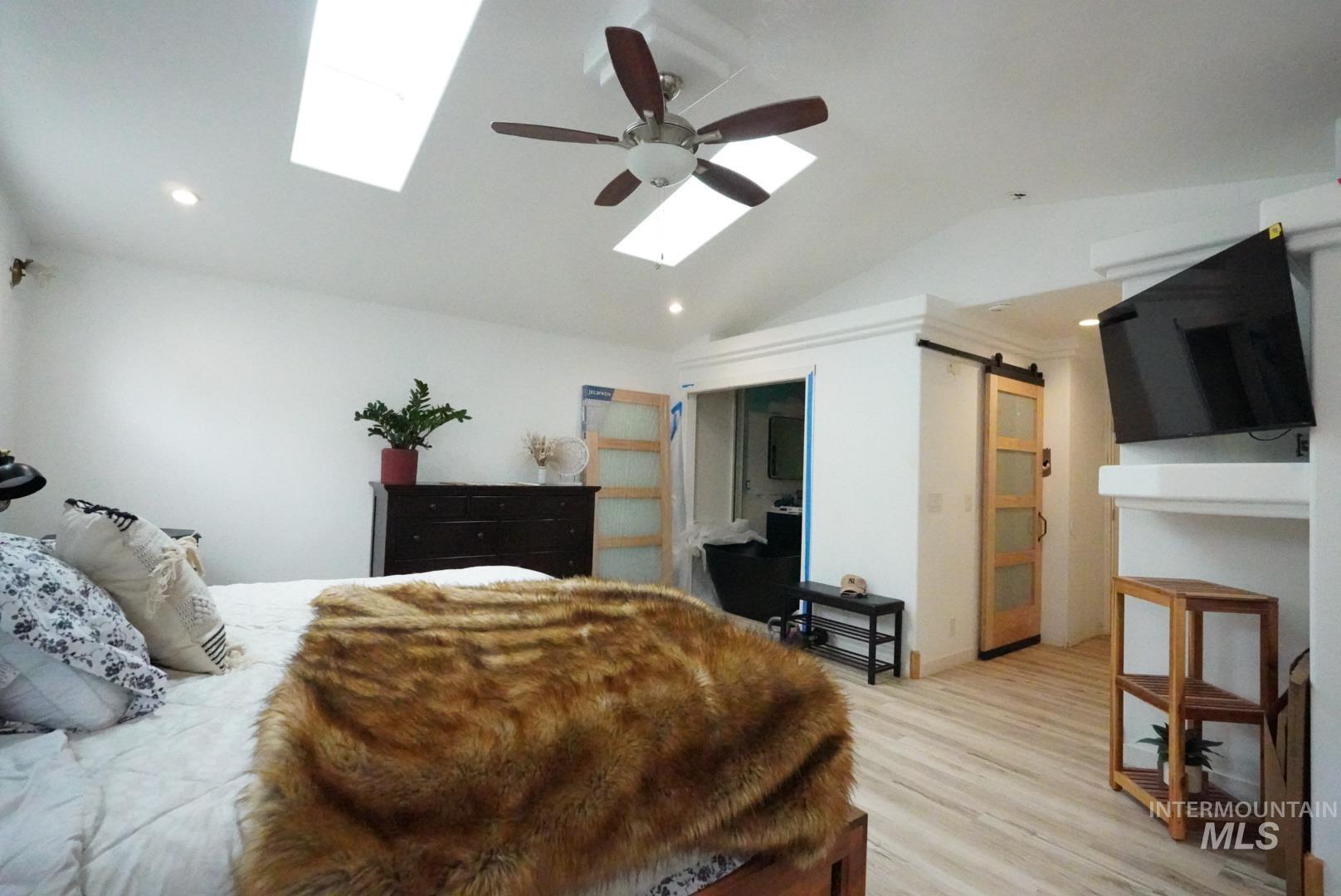 Bedroom with a barn door, vaulted ceiling, light wood-style floors, a skylight, and a ceiling fan