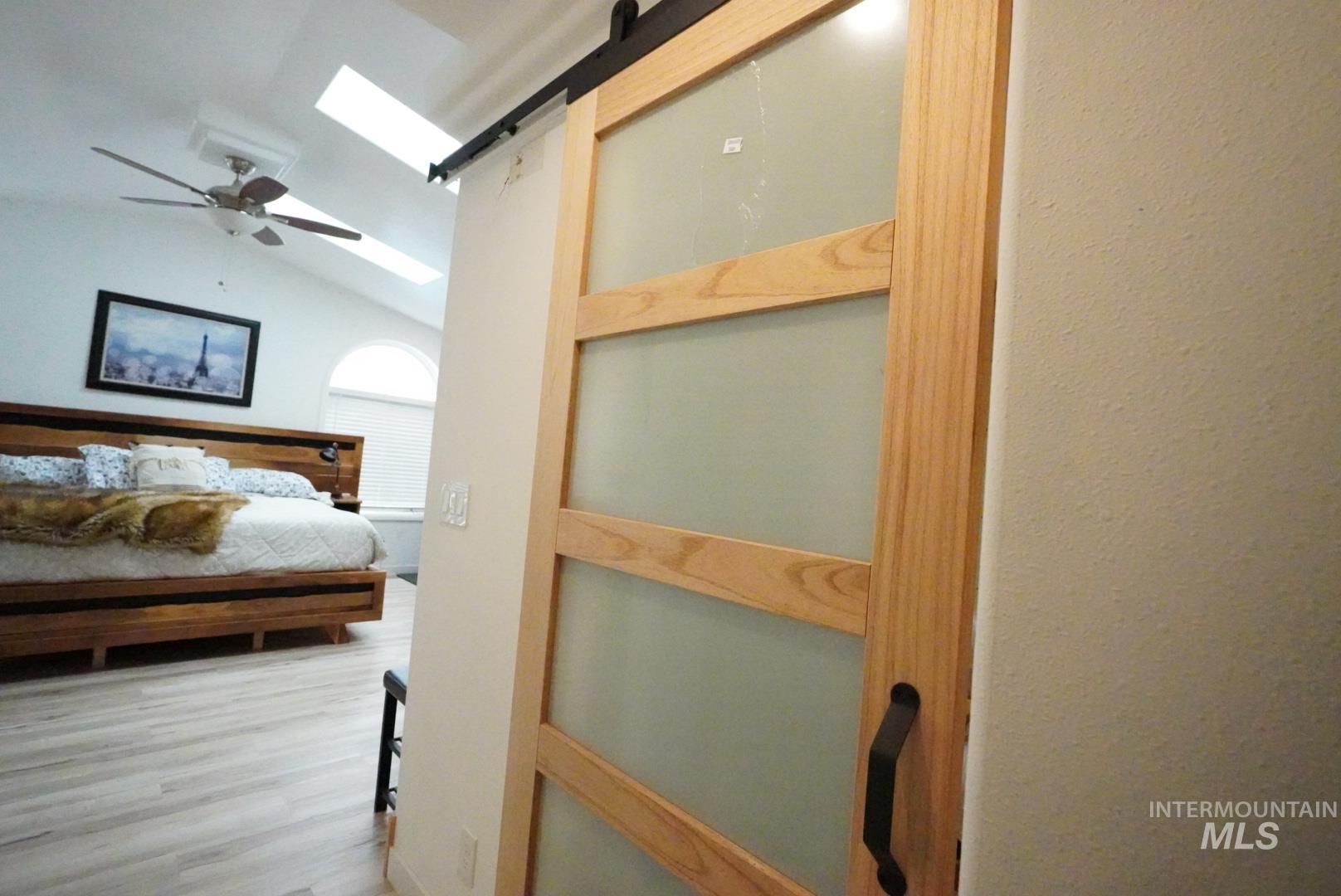 Bedroom with a skylight, vaulted ceiling, wood finished floors, and a ceiling fan