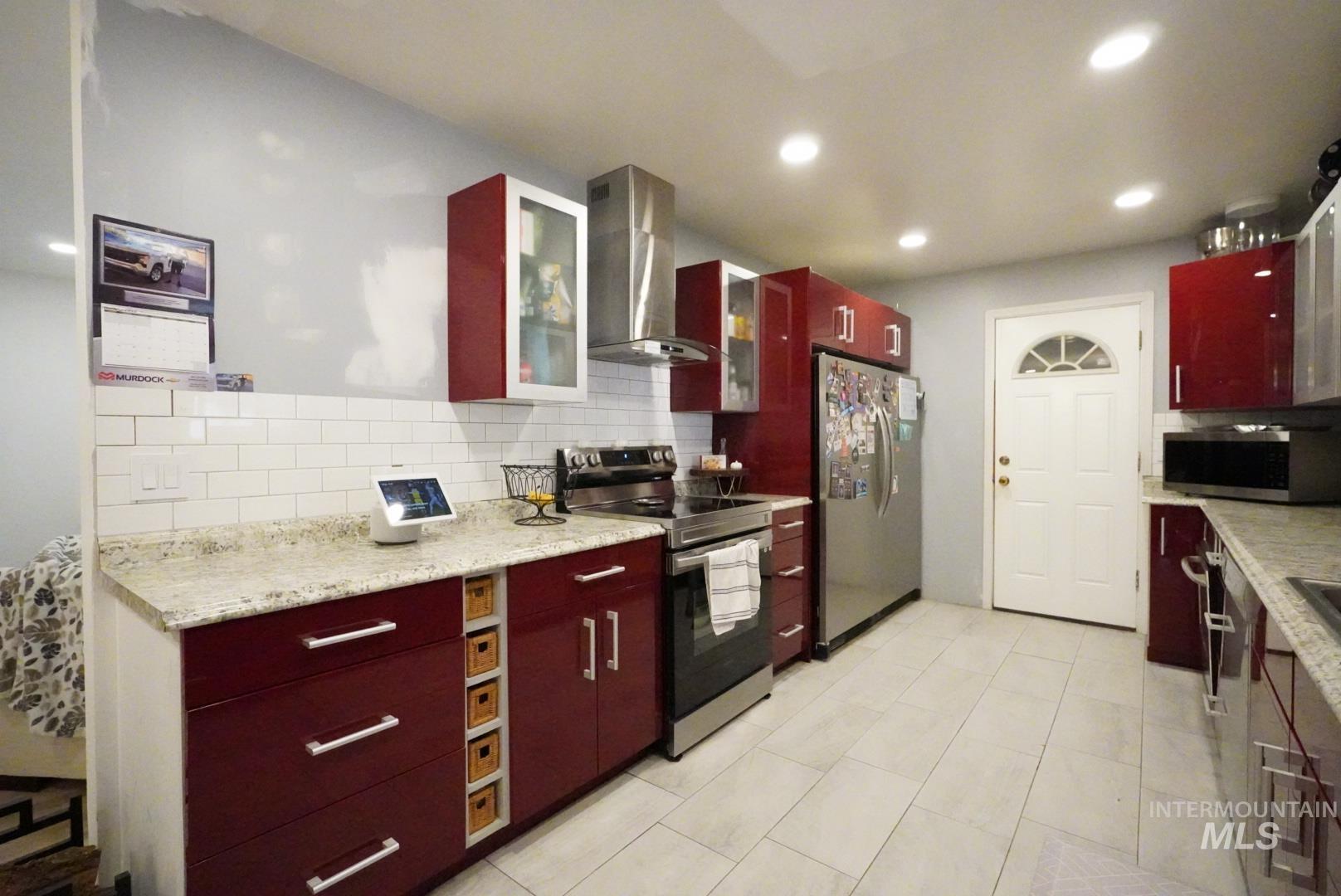 Kitchen with stainless steel appliances, tasteful backsplash, wall chimney exhaust hood, dark brown cabinets, and glass insert cabinets