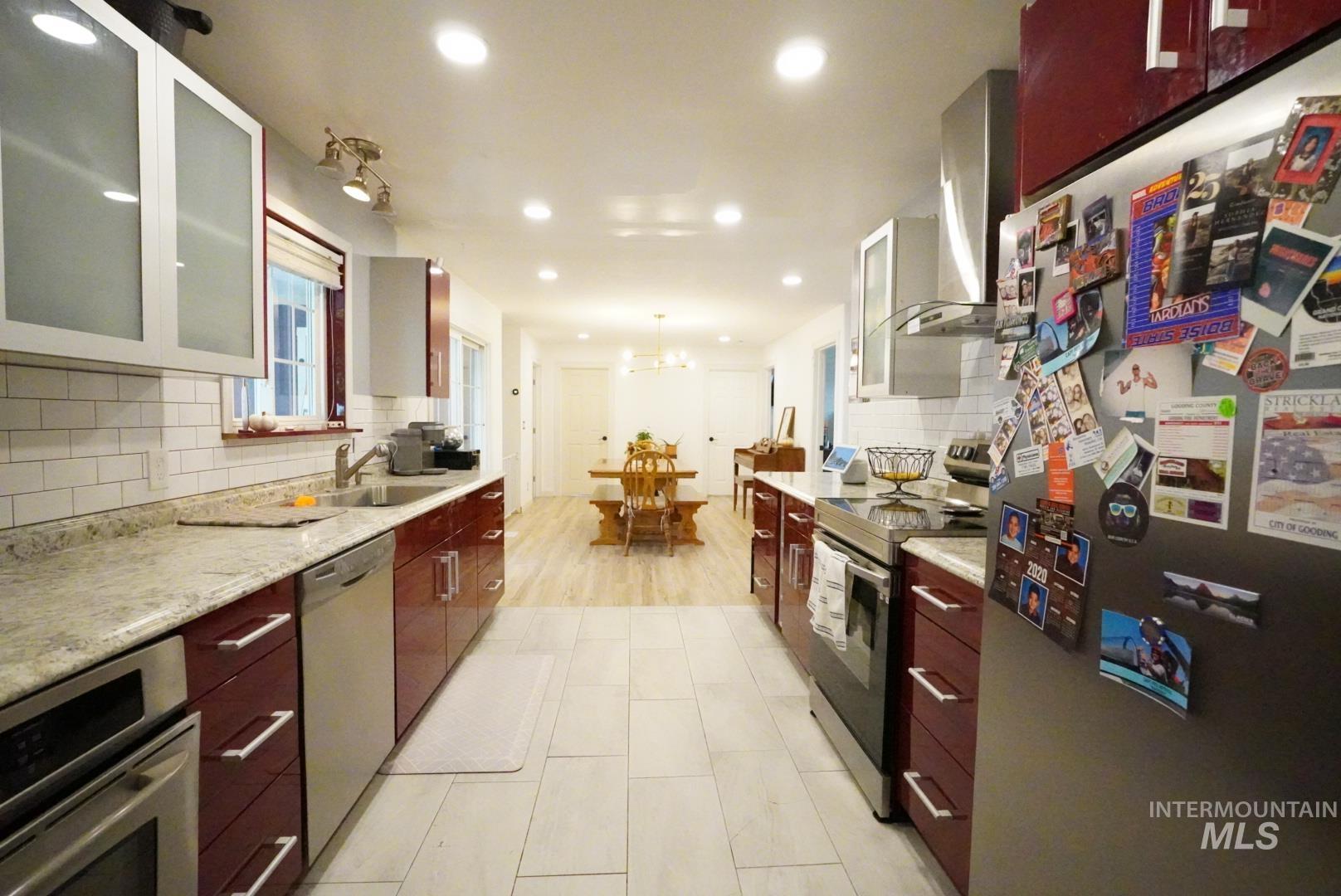 Kitchen featuring glass insert cabinets, appliances with stainless steel finishes, tasteful backsplash, wall chimney range hood, and recessed lighting