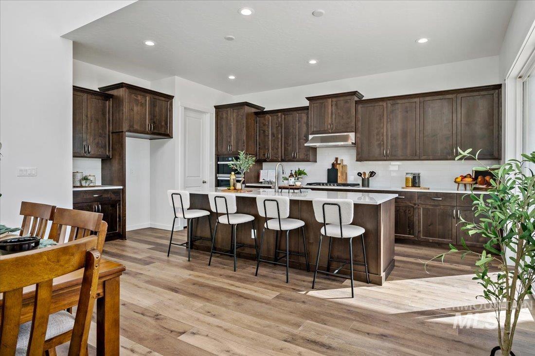 Kitchen with recessed lighting, a kitchen breakfast bar, backsplash, light wood-style flooring, and dark brown cabinetry