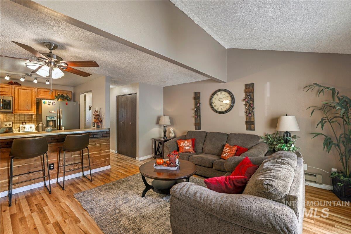 Living area with a textured ceiling, light wood finished floors, a ceiling fan, and a baseboard heating unit