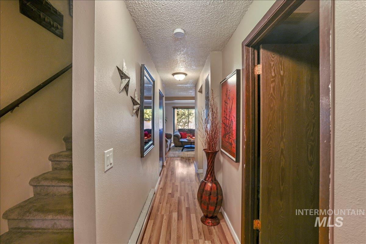 Corridor featuring a textured ceiling, a textured wall, and light wood finished floors