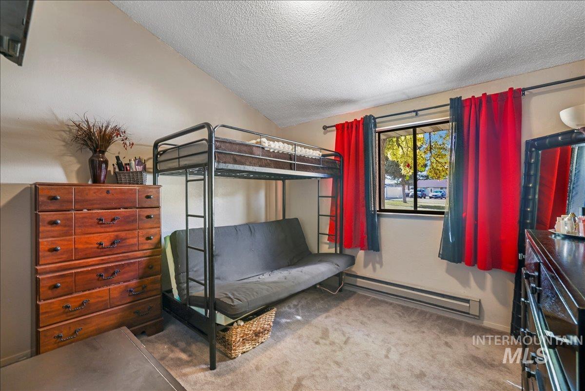 Bedroom featuring a baseboard heating unit, light colored carpet, a textured ceiling, and lofted ceiling
