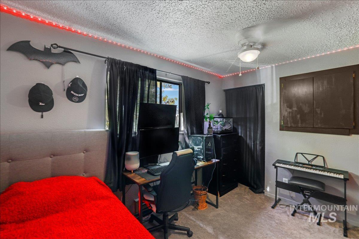 Bedroom featuring a textured ceiling, light colored carpet, an office area, and ceiling fan