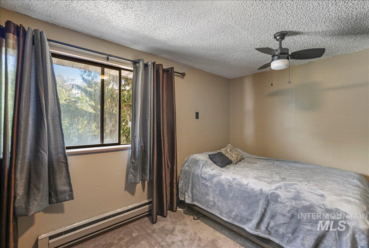 Bedroom featuring baseboard heating, carpet flooring, a textured ceiling, a textured wall, and a ceiling fan