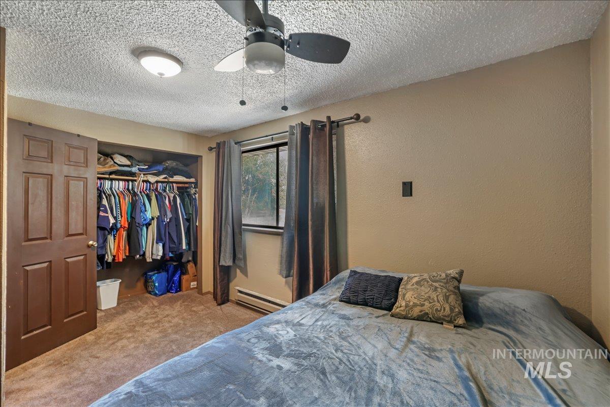 Carpeted bedroom with a textured ceiling, a closet, baseboard heating, ceiling fan, and a textured wall