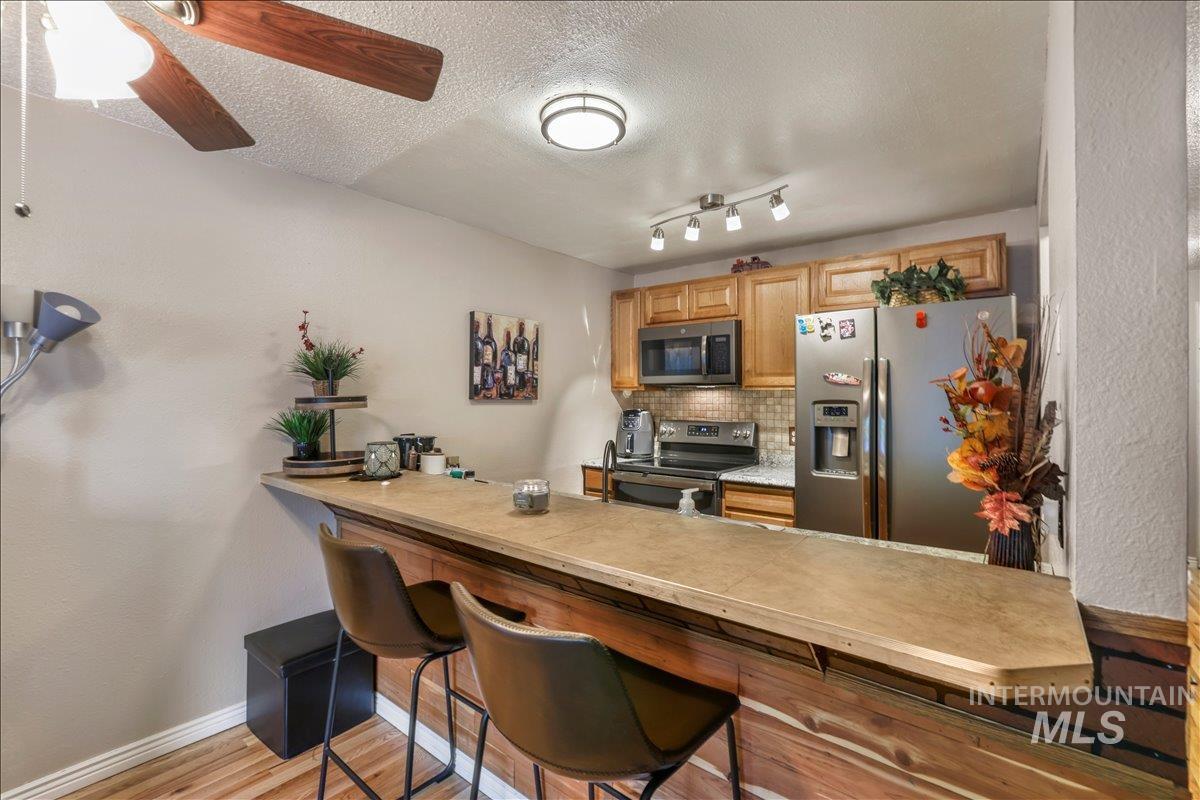Kitchen with appliances with stainless steel finishes, backsplash, light wood-style flooring, a kitchen breakfast bar, and a textured ceiling