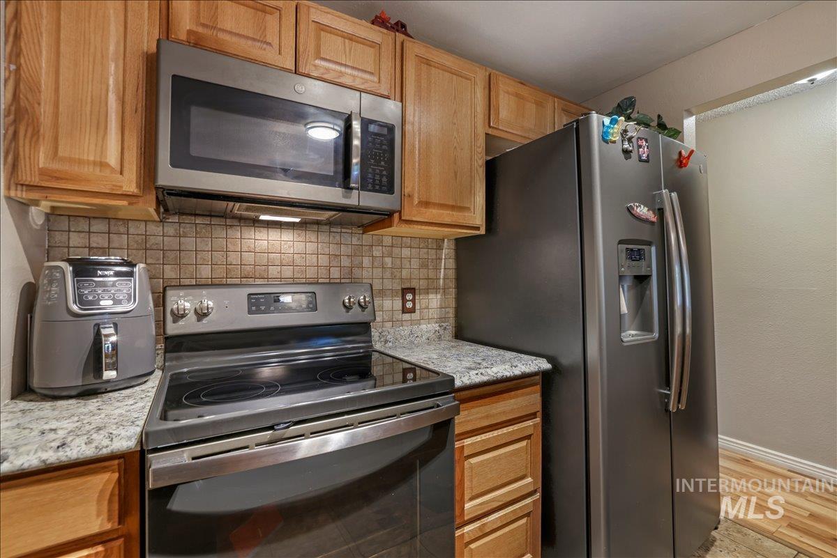Kitchen with appliances with stainless steel finishes, backsplash, light stone counters, and light wood-style flooring