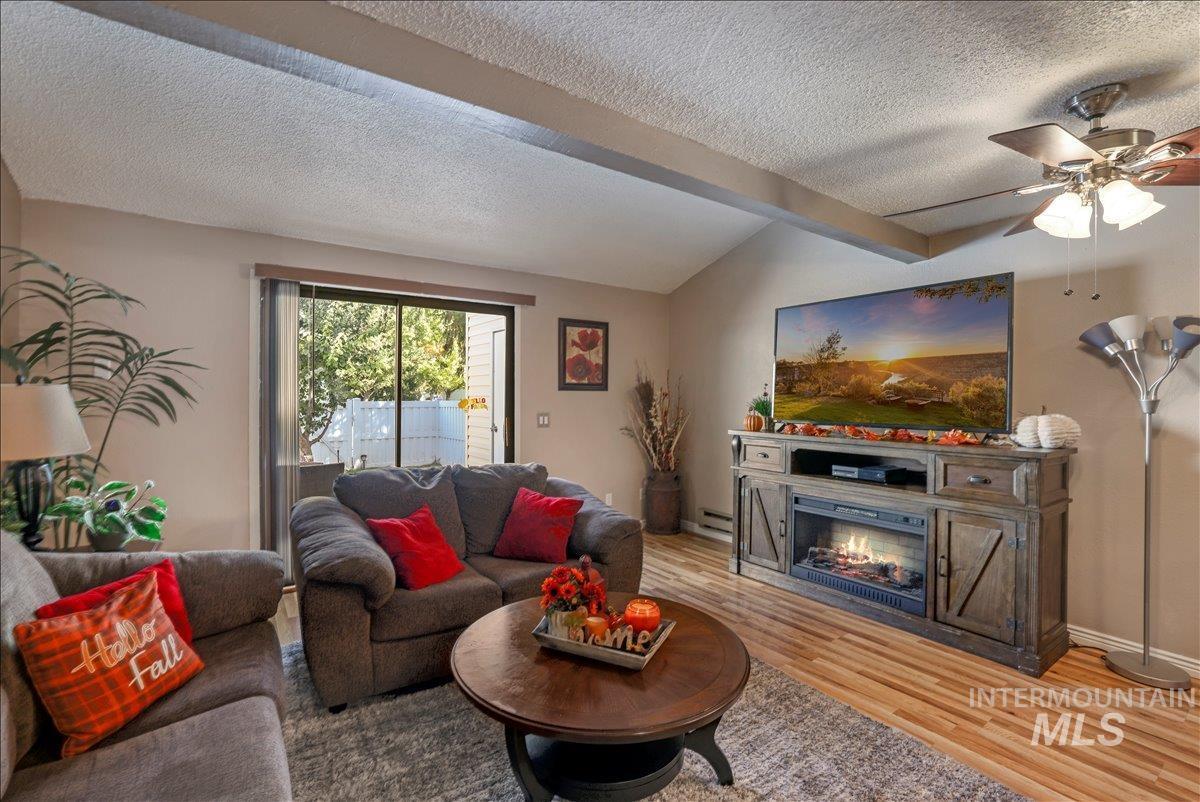 Living area featuring wood finished floors, a textured ceiling, a ceiling fan, and a lit fireplace