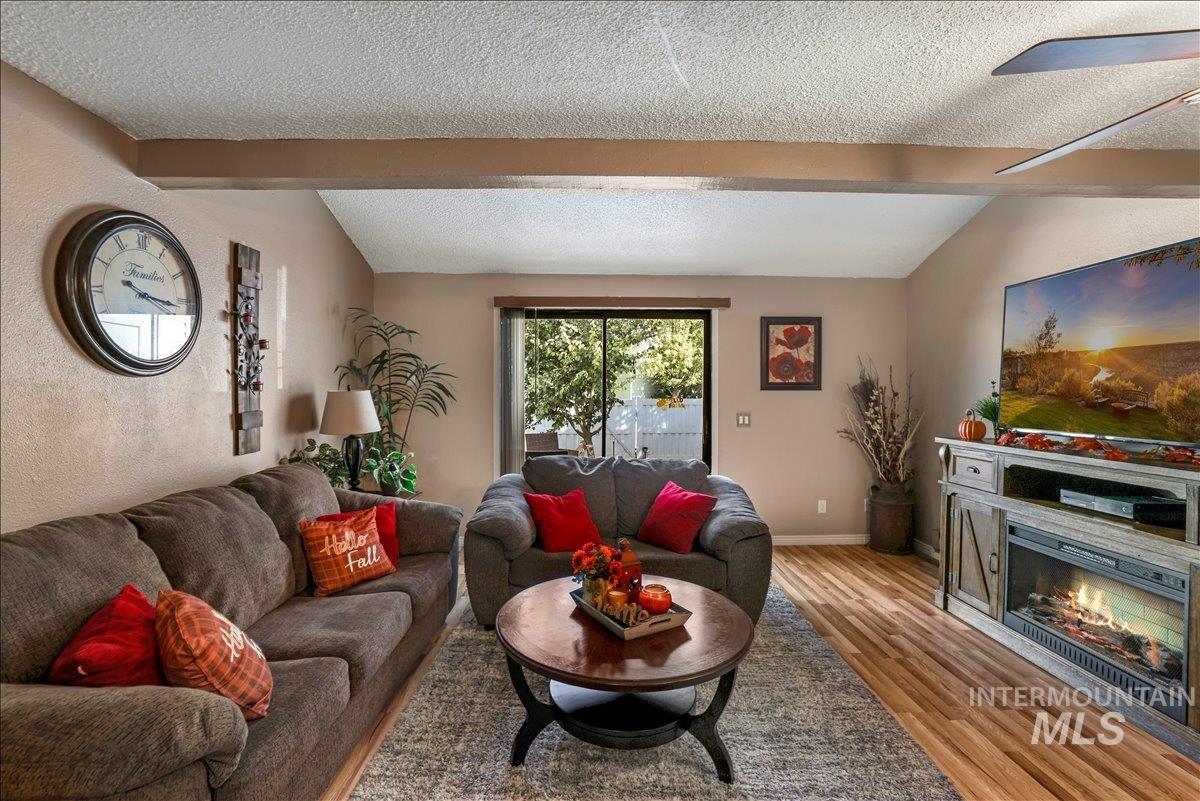 Living room with a textured ceiling, light wood-style flooring, a glass covered fireplace, and a textured wall