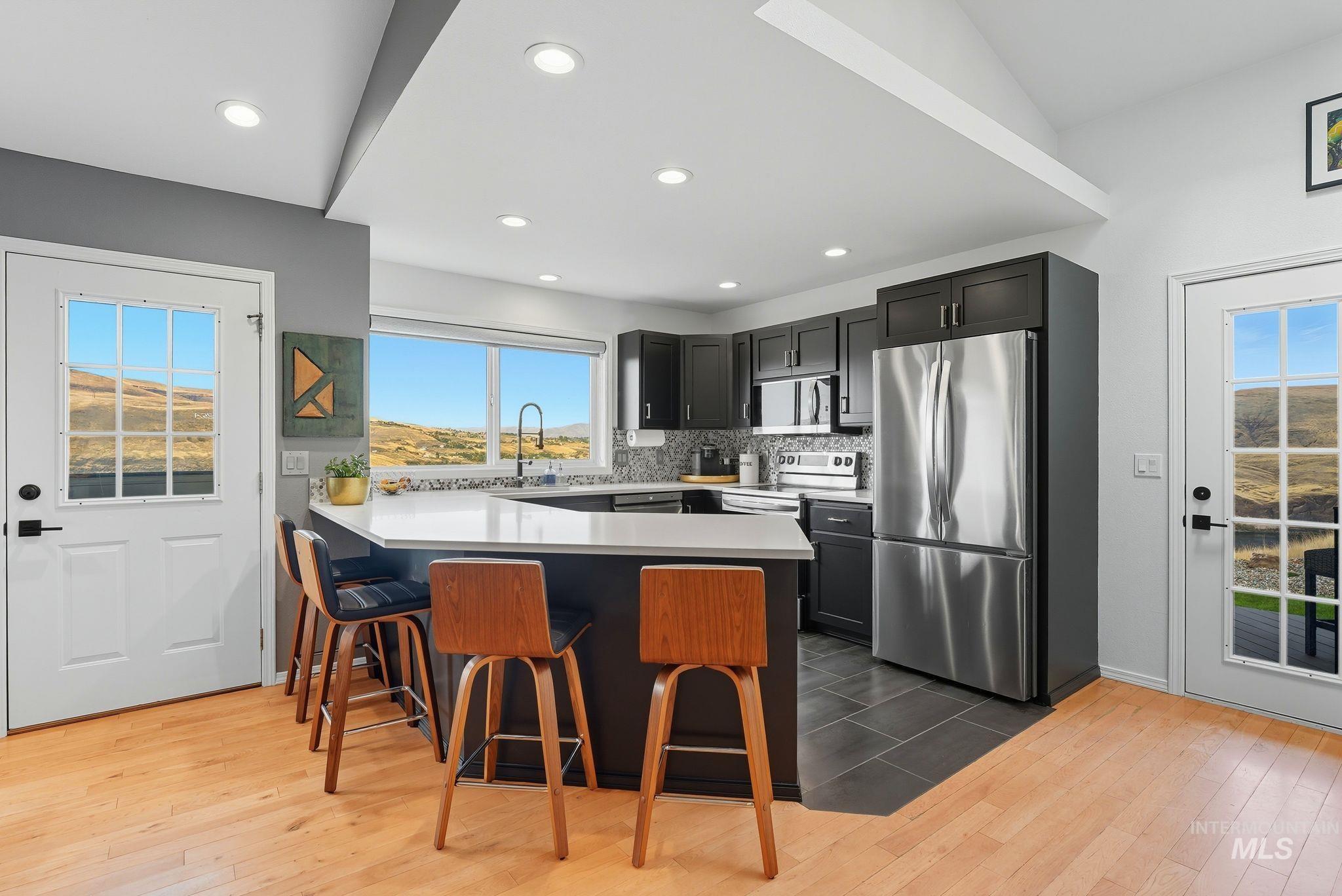 Kitchen featuring a peninsula, a breakfast bar, appliances with stainless steel finishes, dark wood-style floors, and decorative backsplash