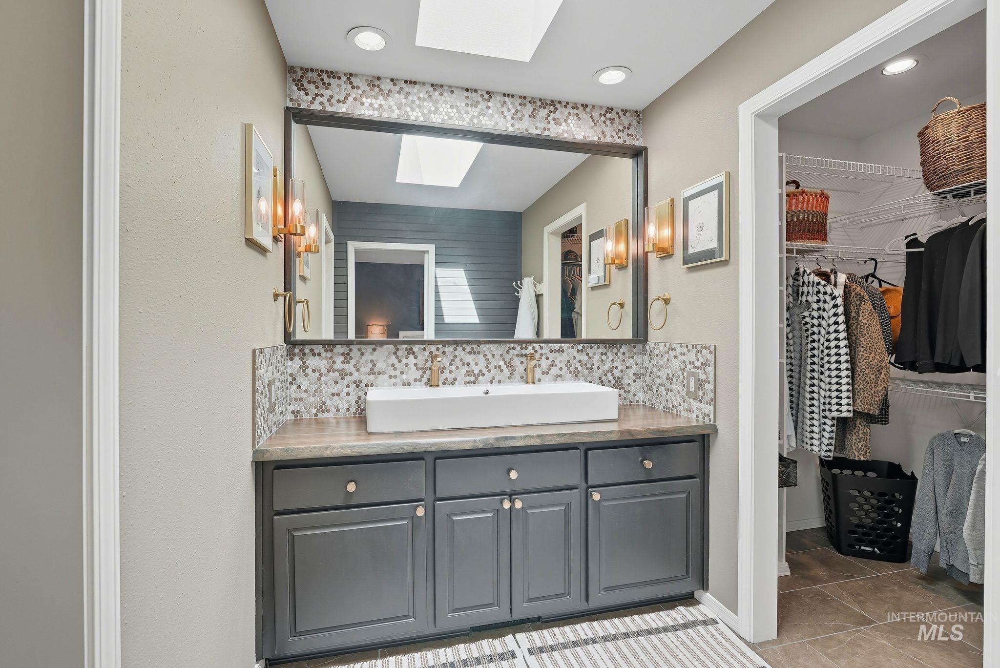 Bathroom featuring a skylight, tasteful backsplash, vanity, a spacious closet, and recessed lighting