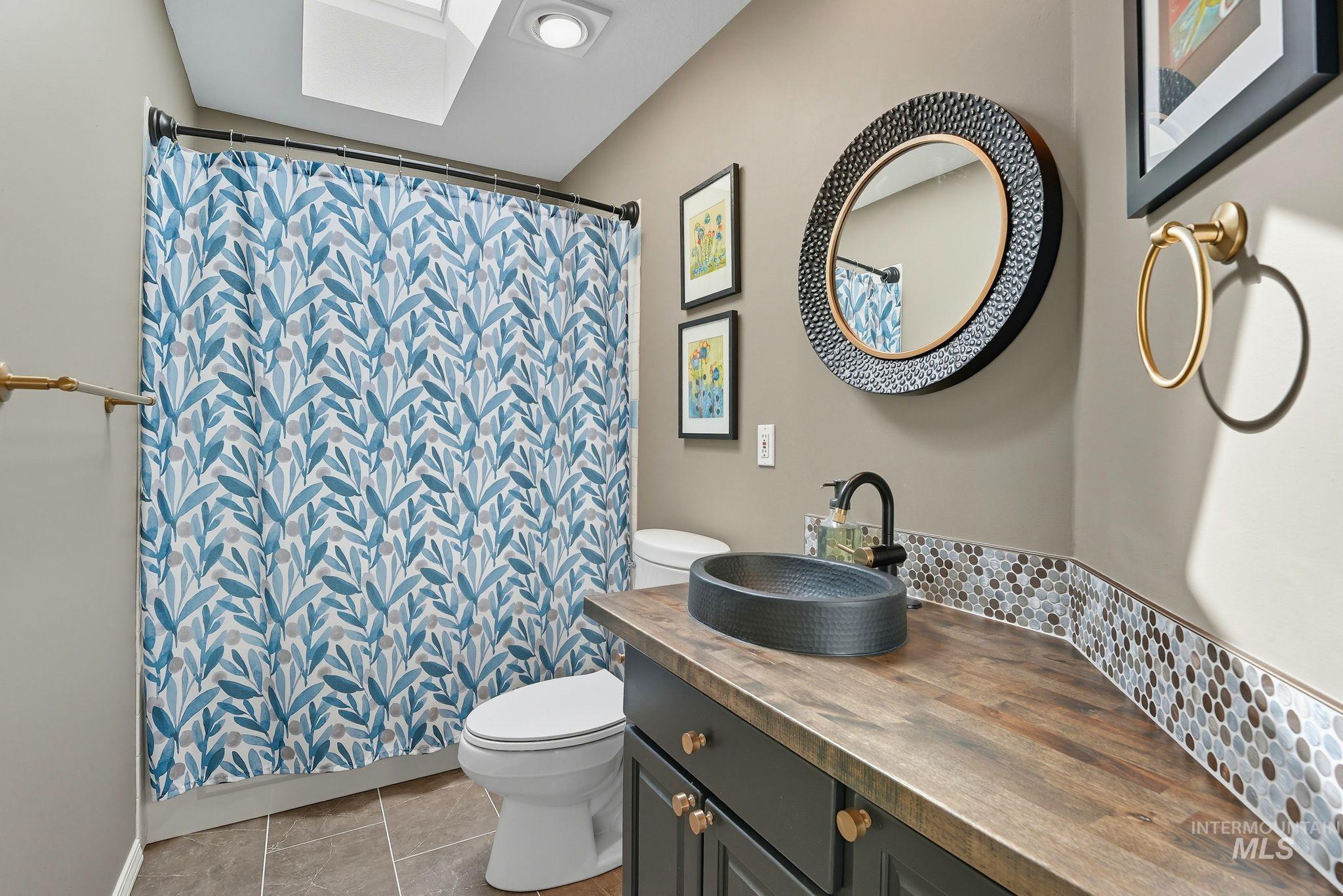 Bathroom featuring vanity, a skylight, light tile patterned floors, curtained shower, and backsplash
