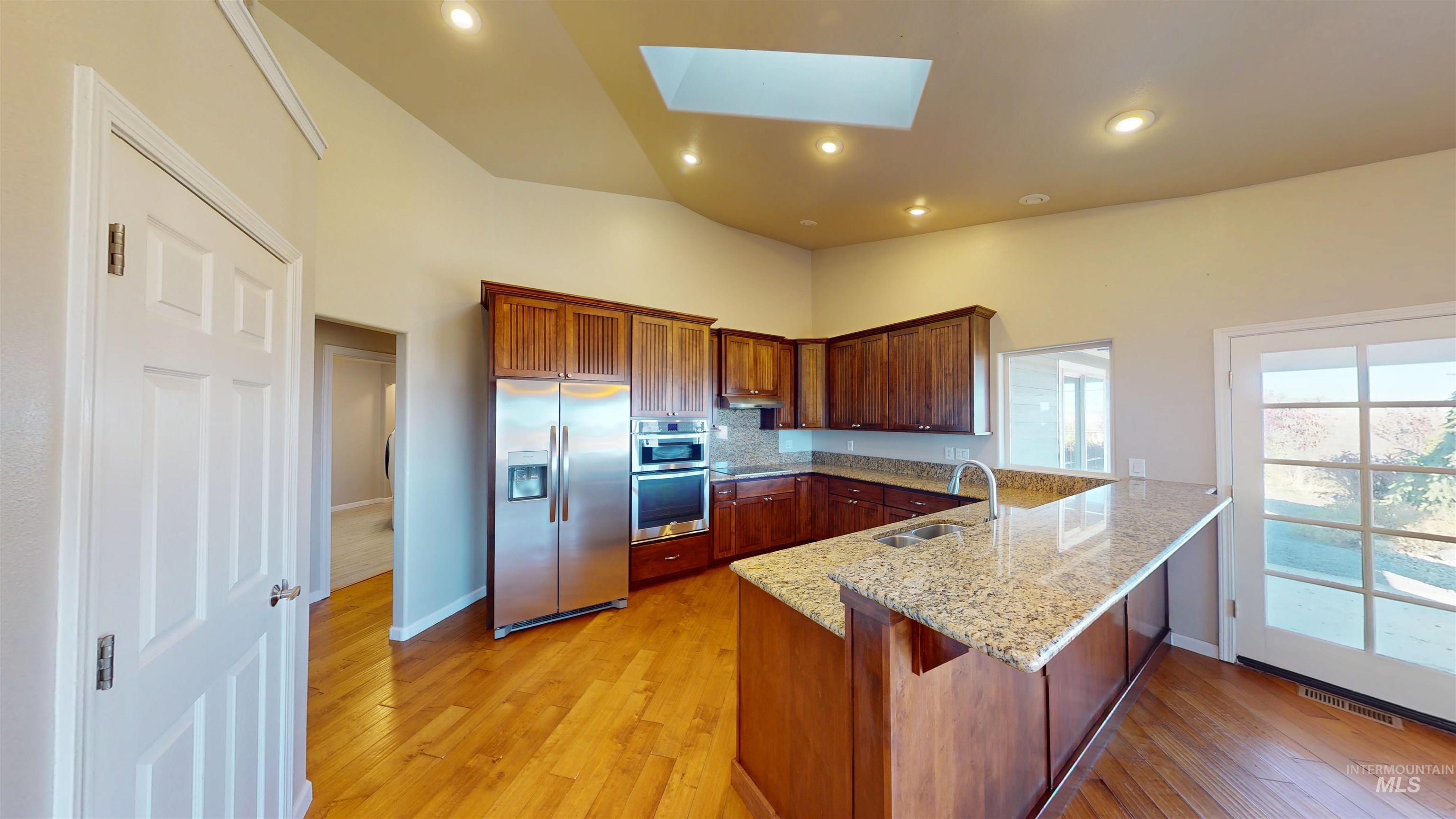 Kitchen featuring a peninsula, appliances with stainless steel finishes, a skylight, light stone counters, and light wood-style floors