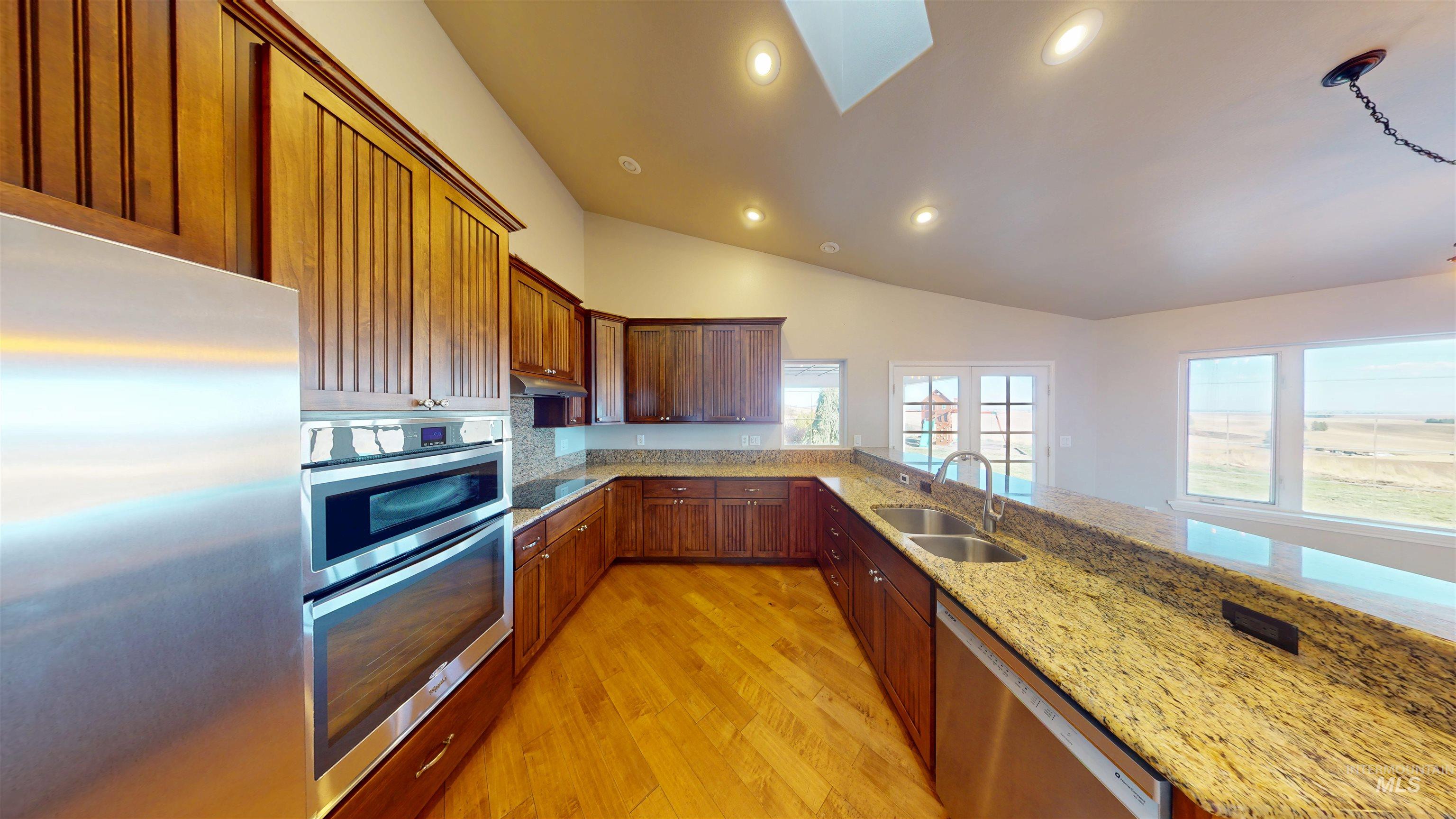 Kitchen featuring stainless steel appliances, light stone counters, a skylight, light wood-type flooring, and recessed lighting