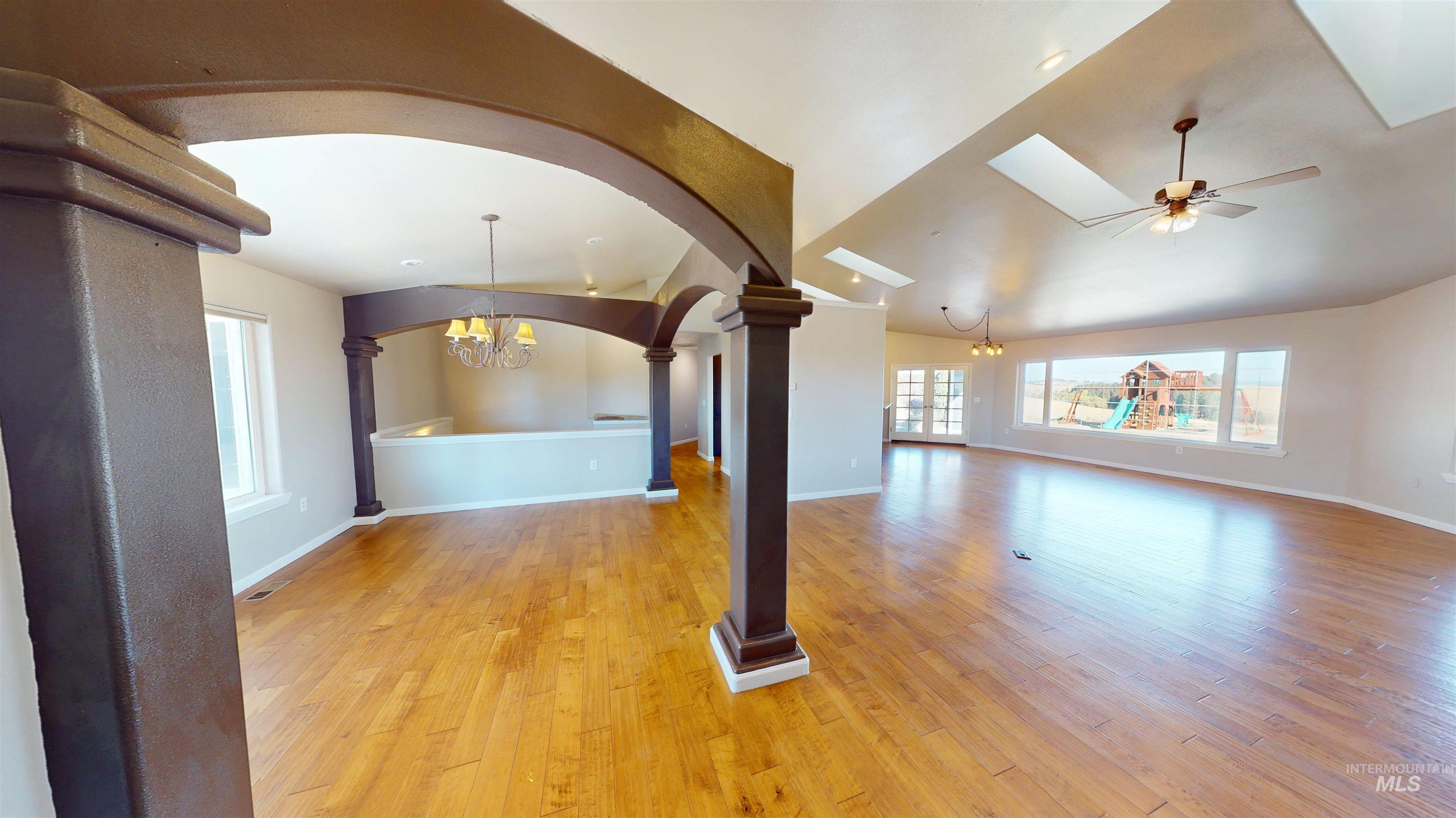 Unfurnished living room with a chandelier, light wood finished floors, arched walkways, lofted ceiling, and a ceiling fan