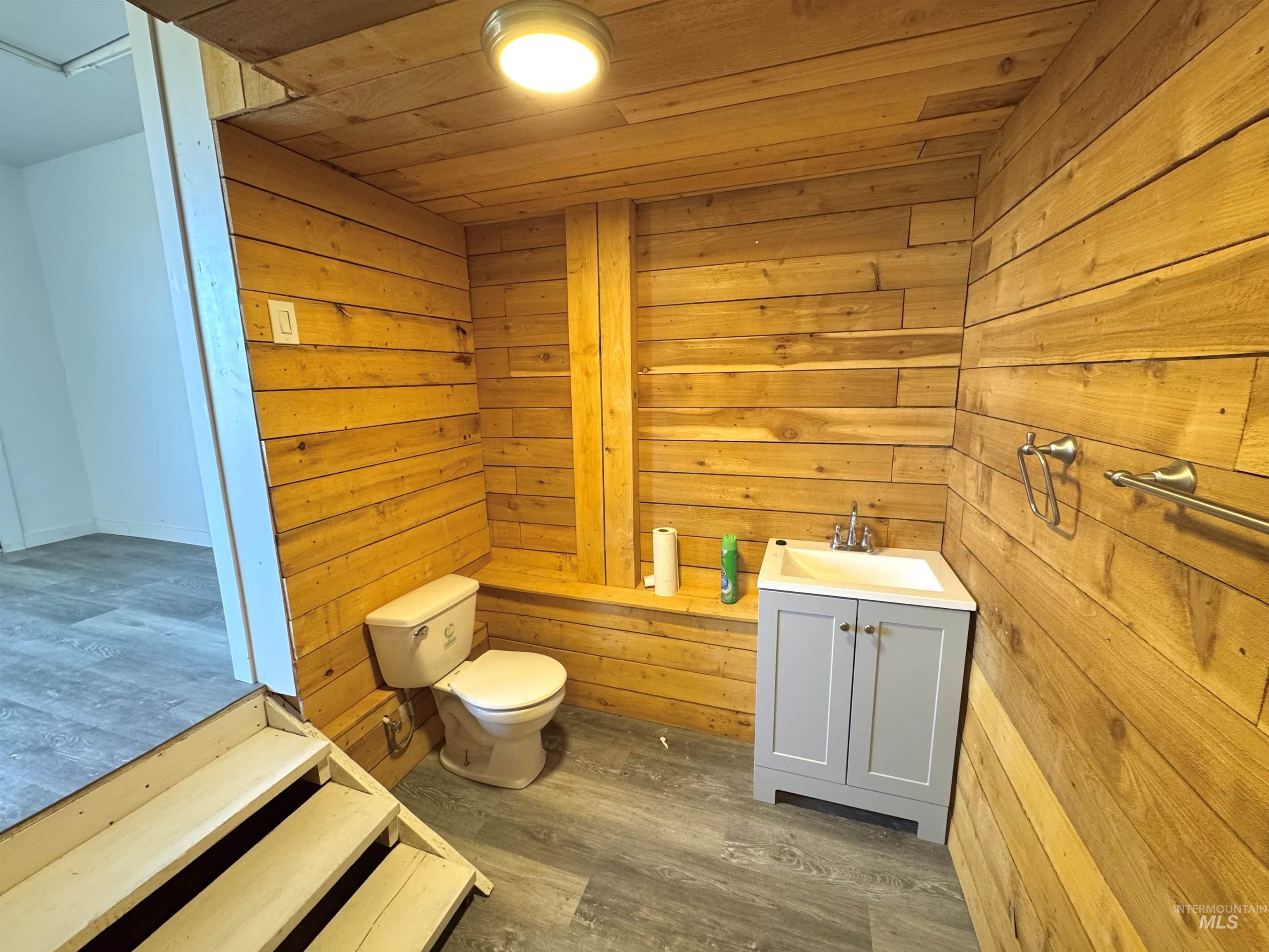 Apartment bathroom featuring vanity, dark wood finished floors, wood walls, and wood ceiling