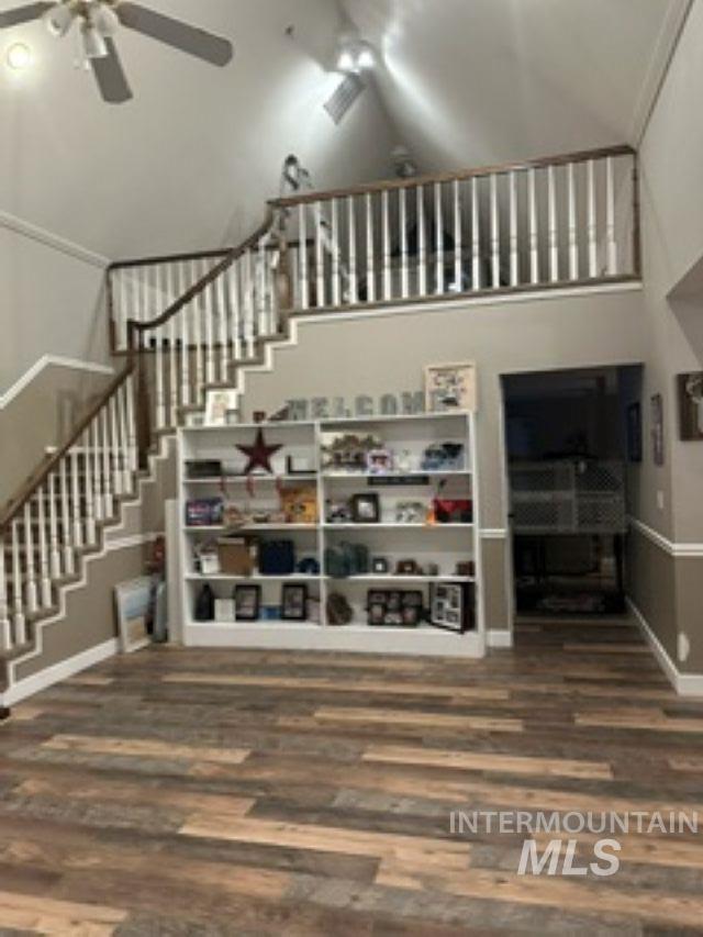Unfurnished living room featuring stairs, a ceiling fan, high vaulted ceiling, and dark wood finished floors
