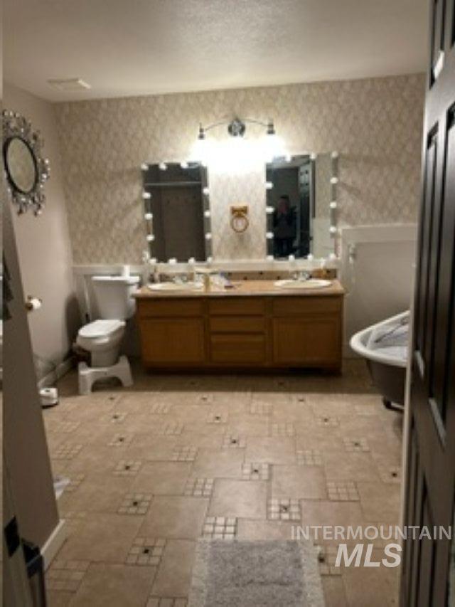 Full bath with wallpapered walls, double vanity, and stone tile flooring