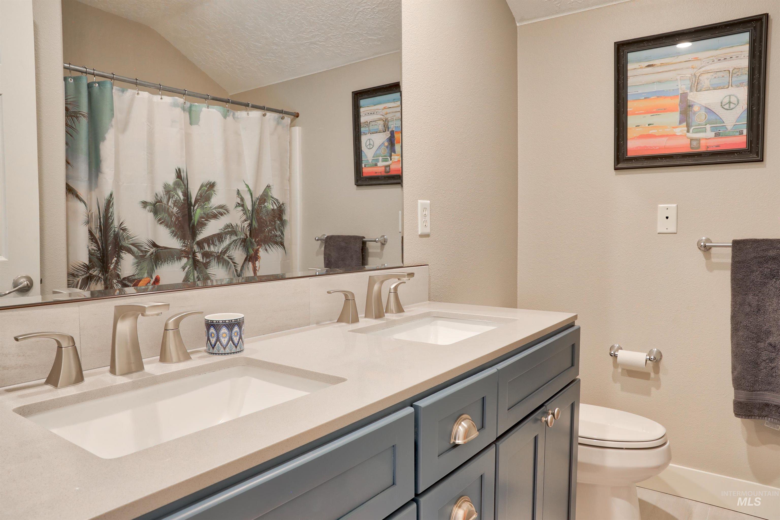 Bathroom with double vanity, a textured ceiling, and curtained shower