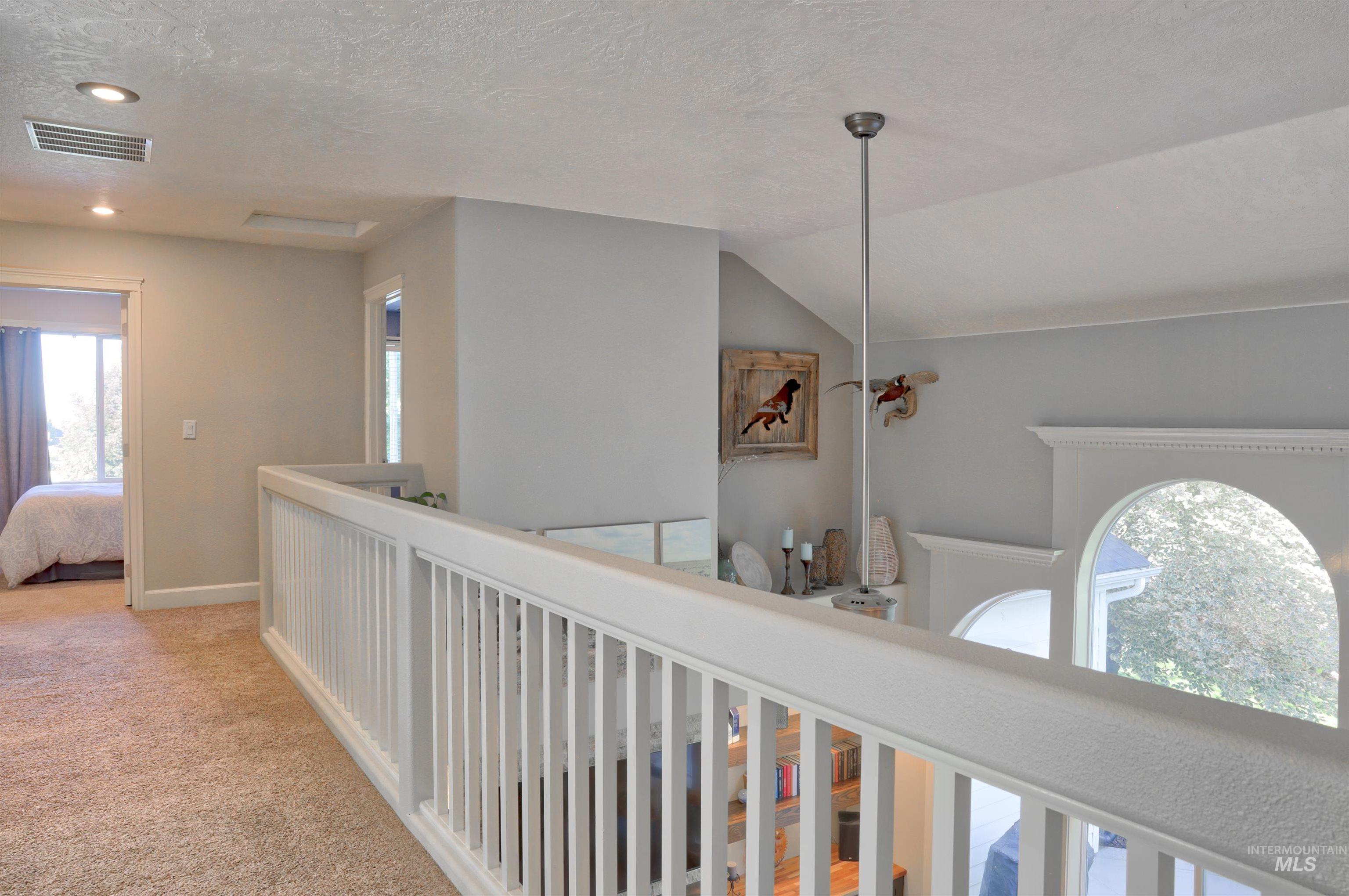 Hall featuring a textured ceiling, light colored carpet, lofted ceiling, and an upstairs landing